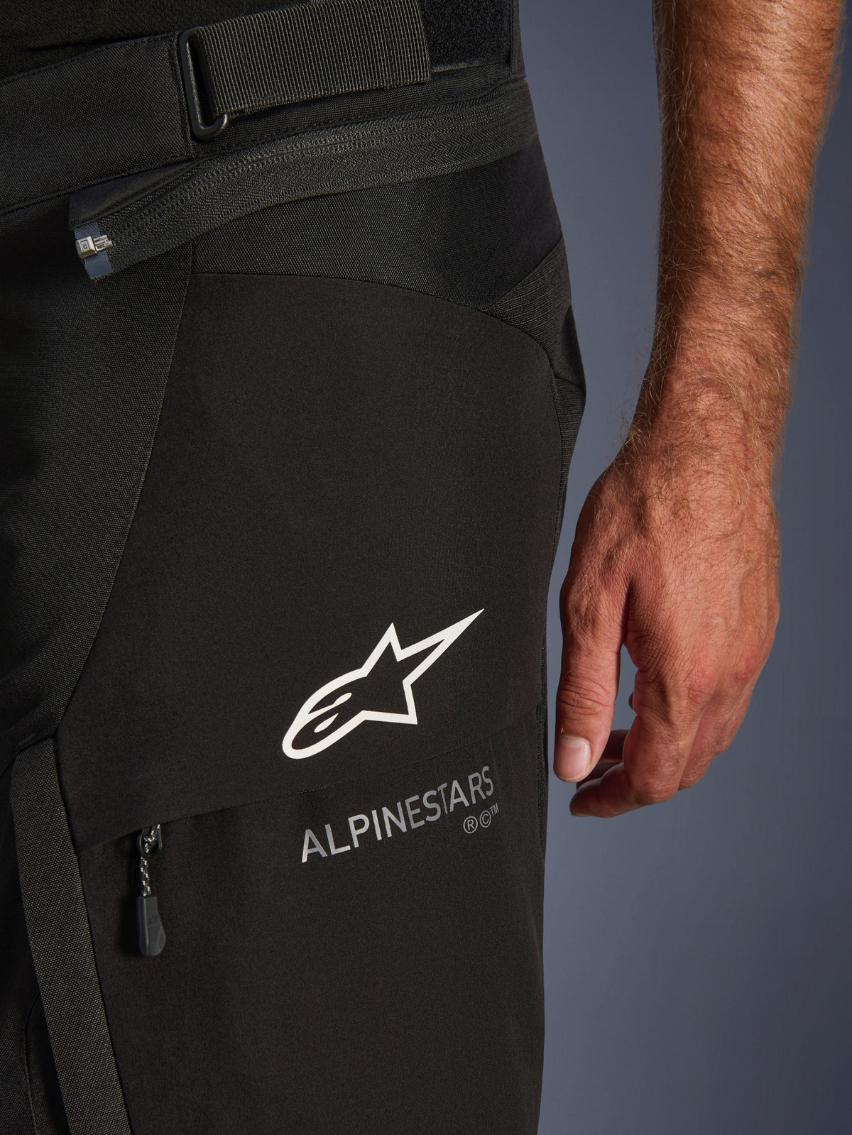 Alpinestars Andes V4 Drystar Pants, Motorcycle Adventure Pants, Black, close-up of the upper thigh area showing the white Alpinestars star logo and text, waist adjustment strap, and zippered pocket detail.