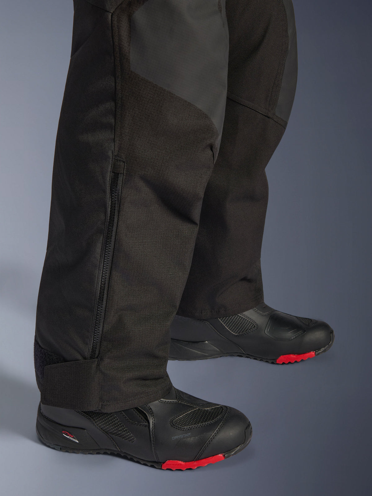 Alpinestars Andes V4 Drystar® Pants, Black adventure motorcycle pants, close-up of lower leg with side zipper detail, durable textile with ripstop reinforcements, worn with black boots featuring red soles