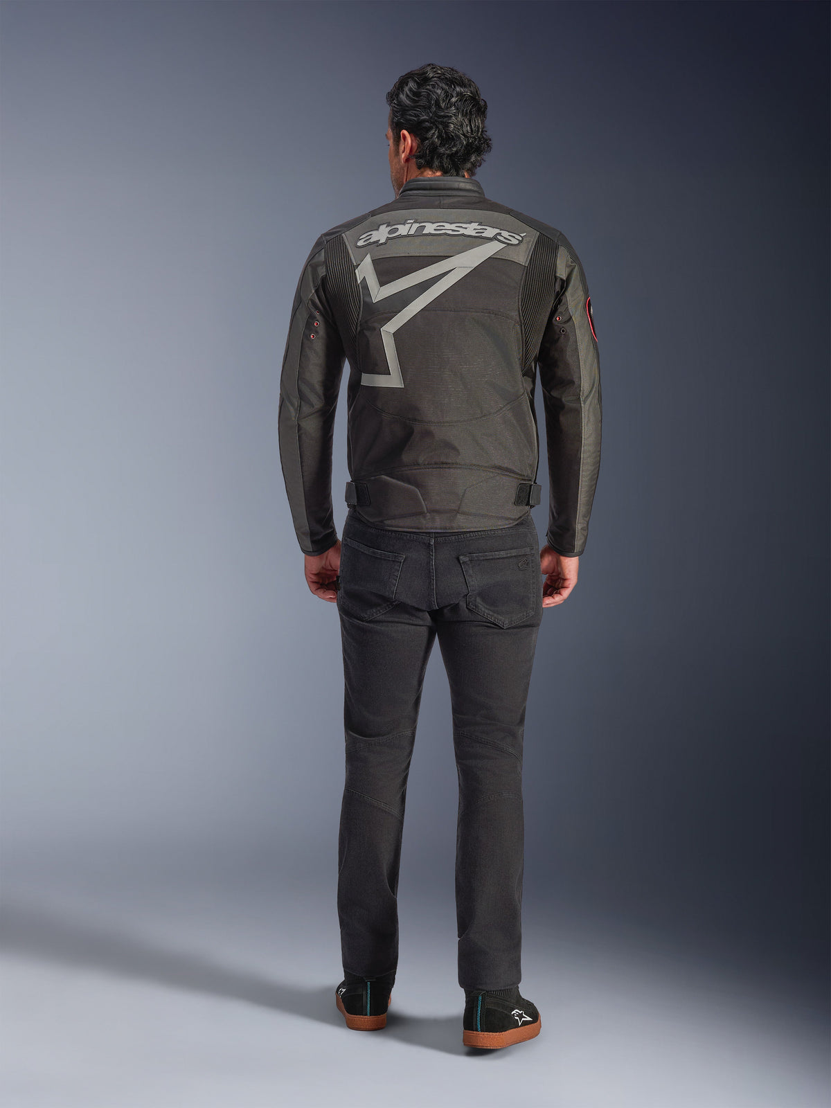 Alpinestars Axton Jacket, Motorcycle Jacket, Black Anthracite Red Tangerine, back view showing large grey Alpinestars logo and star graphic, accordion shoulder panels, worn with black pants and casual black shoes.