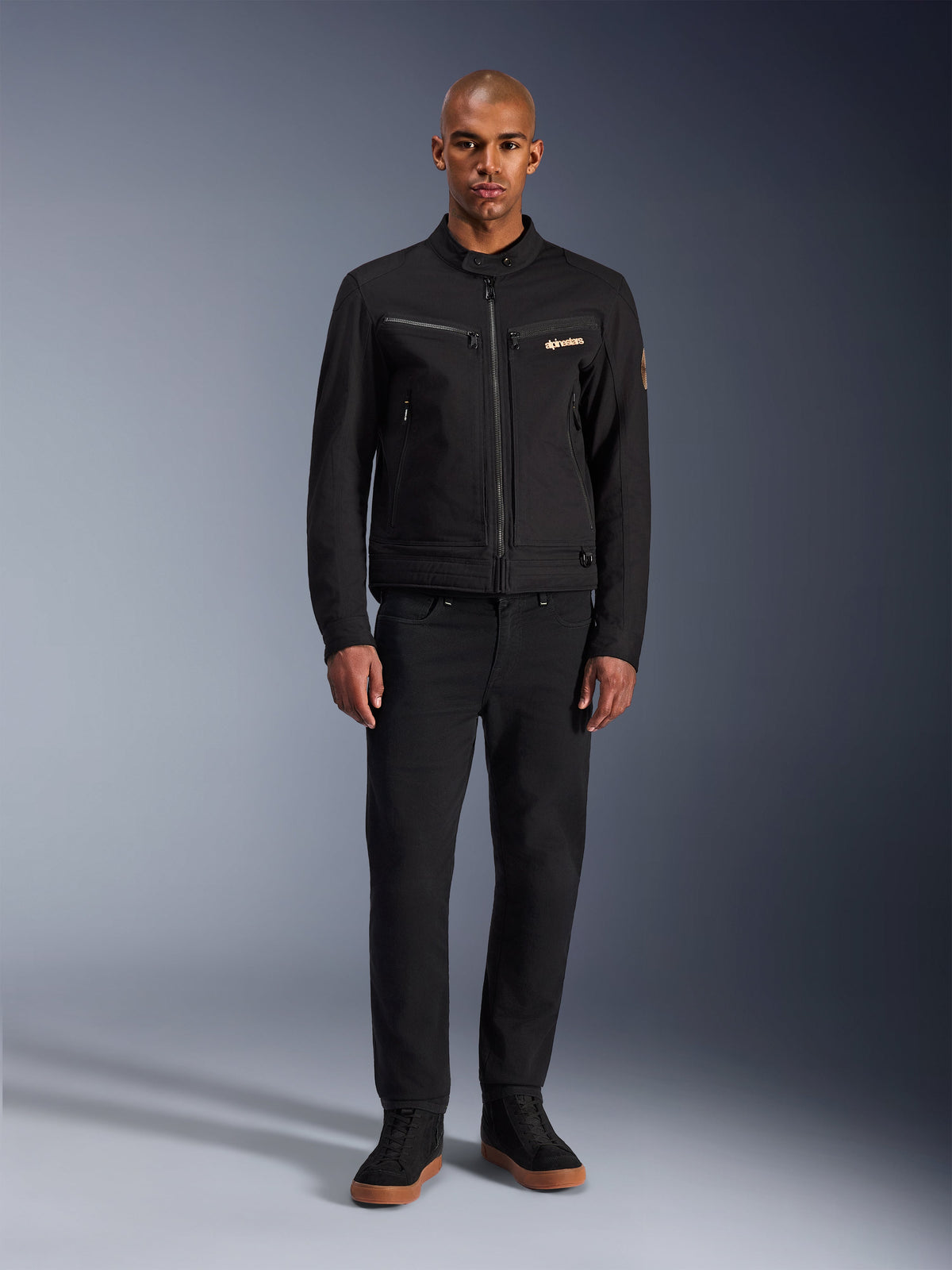 Alpinestars Bruiser Jacket, Black urban motorcycle jacket, worn by model with black pants and high-top sneakers, front view showing zippered chest pockets and embroidered logo, classic workwear-inspired design for everyday commuting