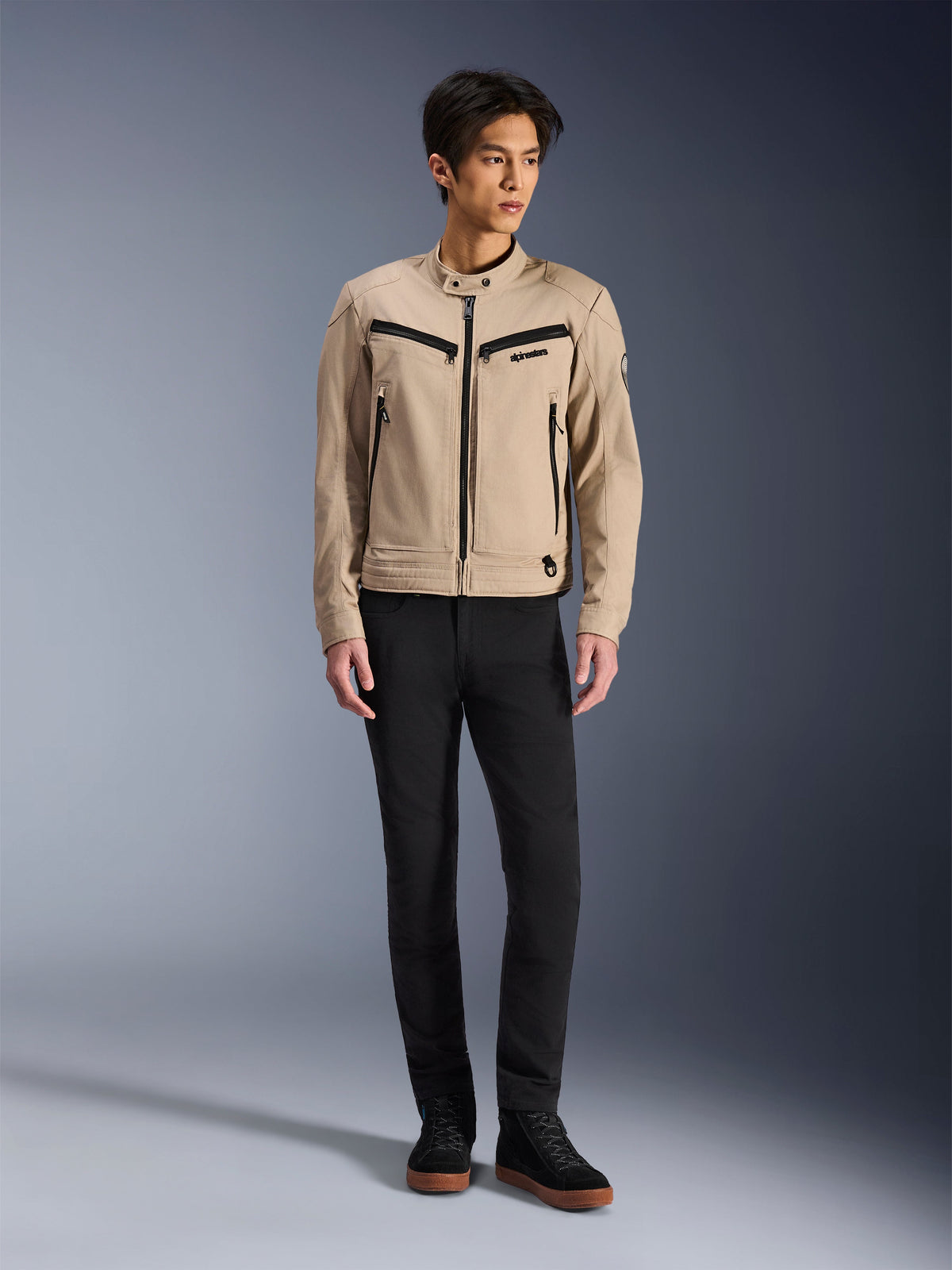 Alpinestars Bruiser Jacket, Urban Motorcycle Jacket in Aluminum, worn with black pants and black sneakers, featuring black zippered pockets and a snap collar, contemporary workwear-inspired design for urban riding