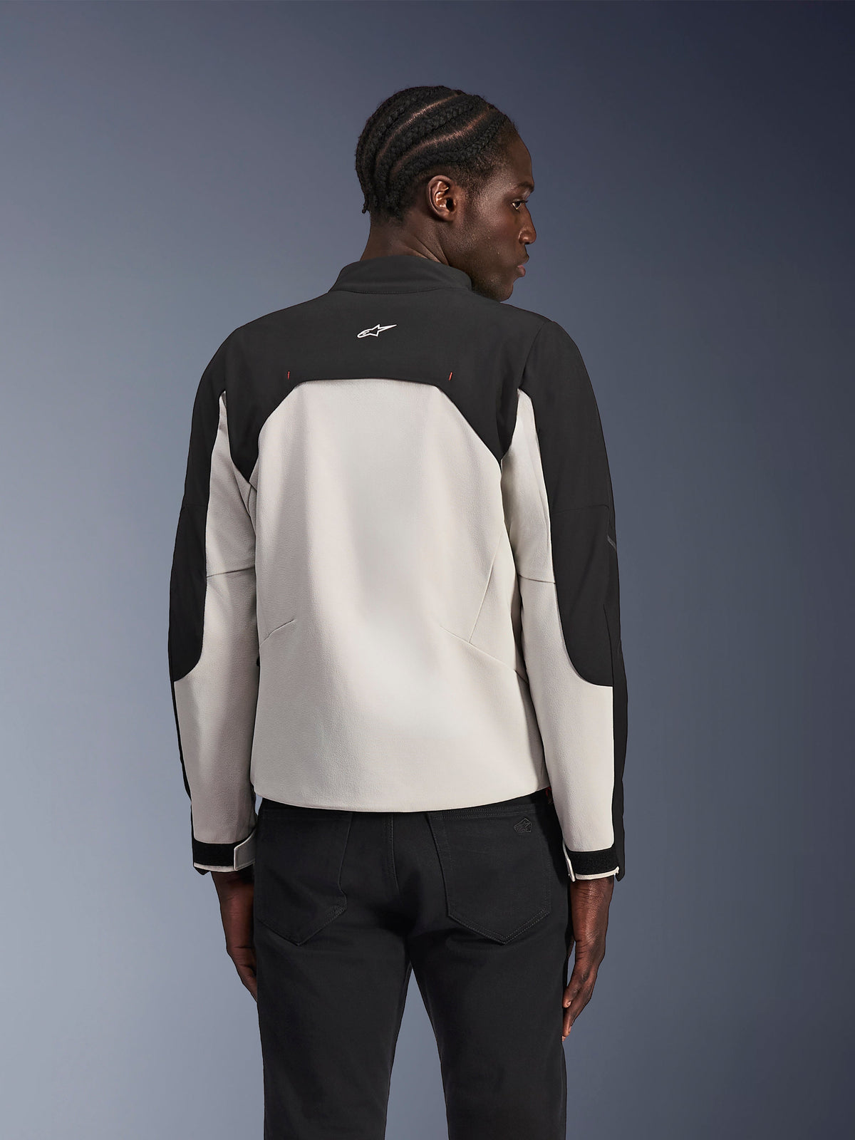 Alpinestars Provoke Jacket, Urban Motorcycle Jacket, Black Metal Gray, back view on a model, featuring a two-tone textile design with black shoulders and light gray back panel, Alpinestars star logo on the back collar, paired with black pants against a blue gradient background