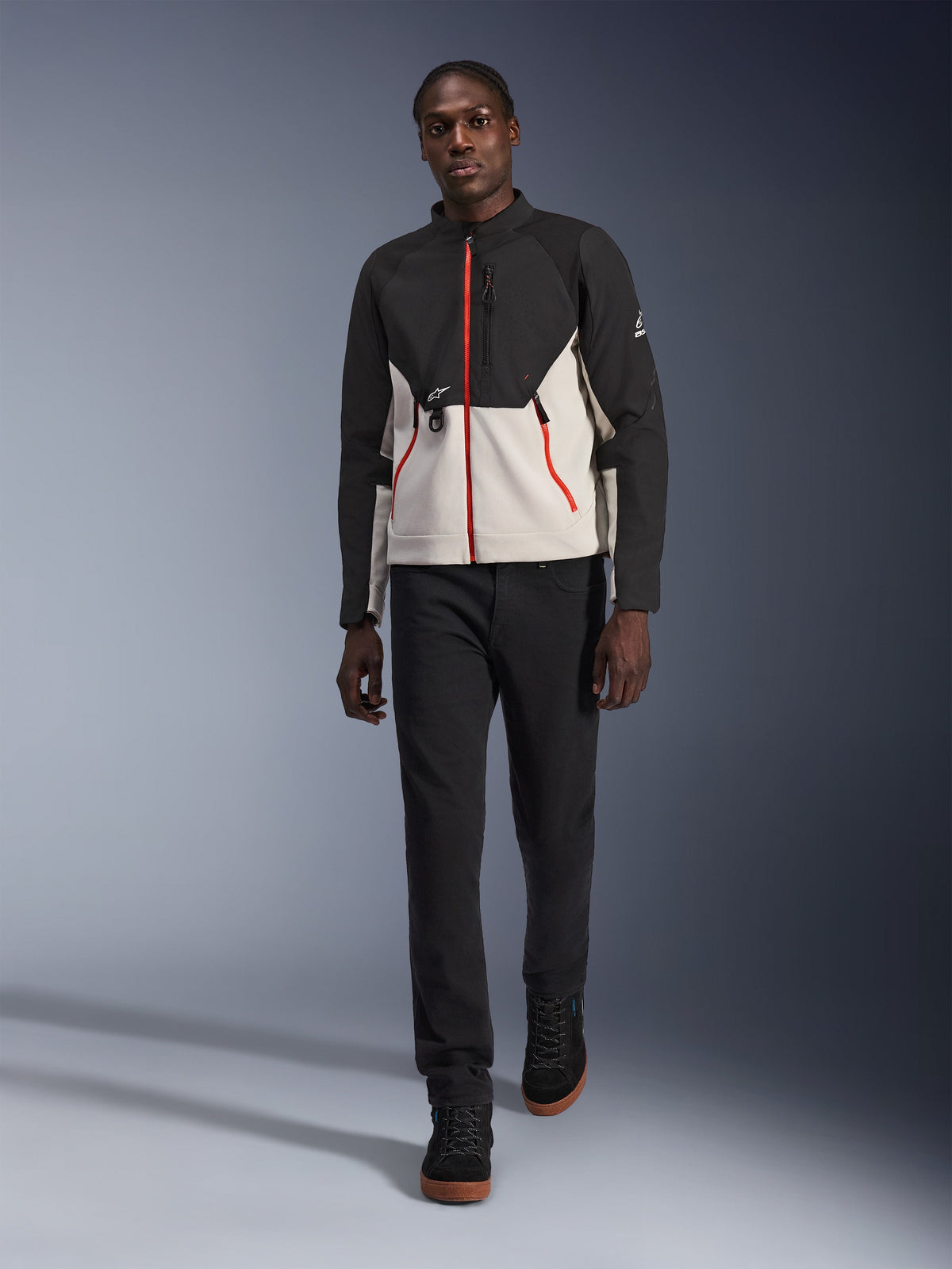 Male model wearing the Alpinestars Provoke Jacket, urban motorcycle jacket in black and metal gray with red zipper accents, paired with black pants and black high-top shoes, modern street-ready protective gear for city riding