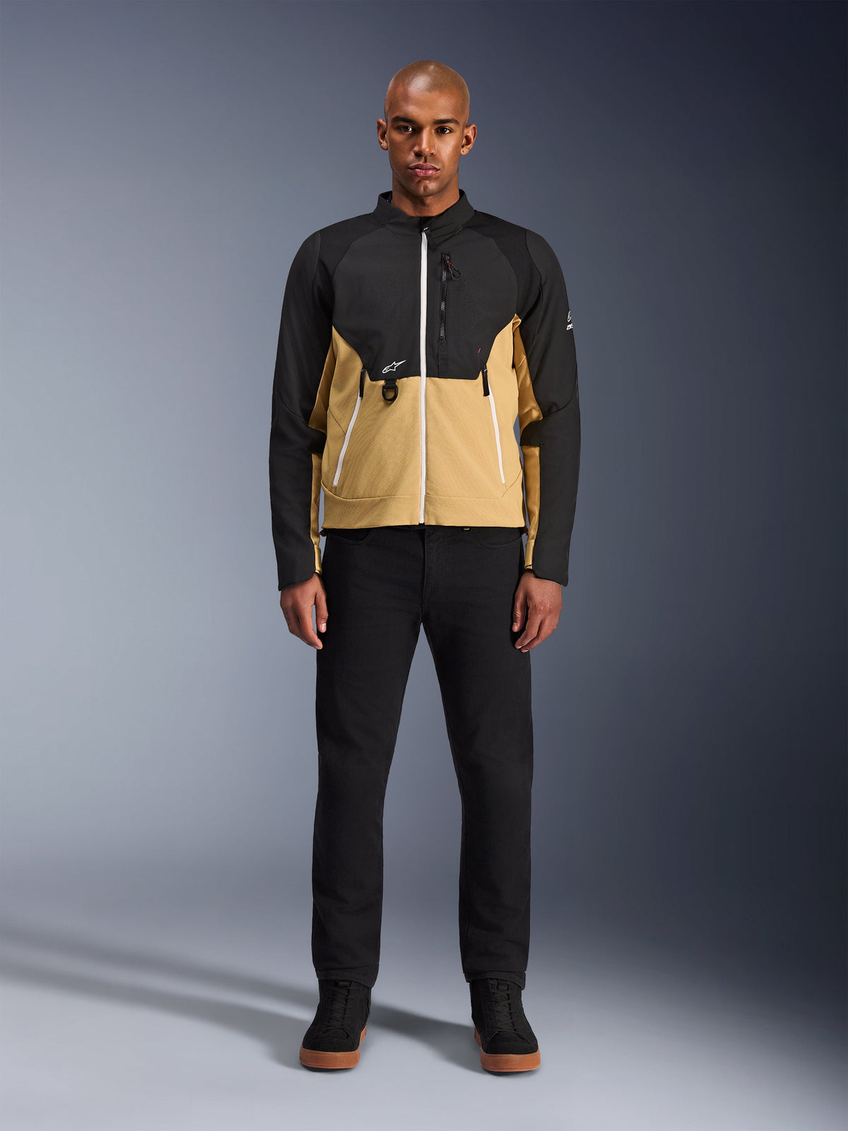 Alpinestars Provoke Jacket in Black Camel, urban motorcycle jacket featuring a two-tone black and camel design, worn by a model with black pants and black shoes, contemporary silhouette with white zippers and technical softshell construction.