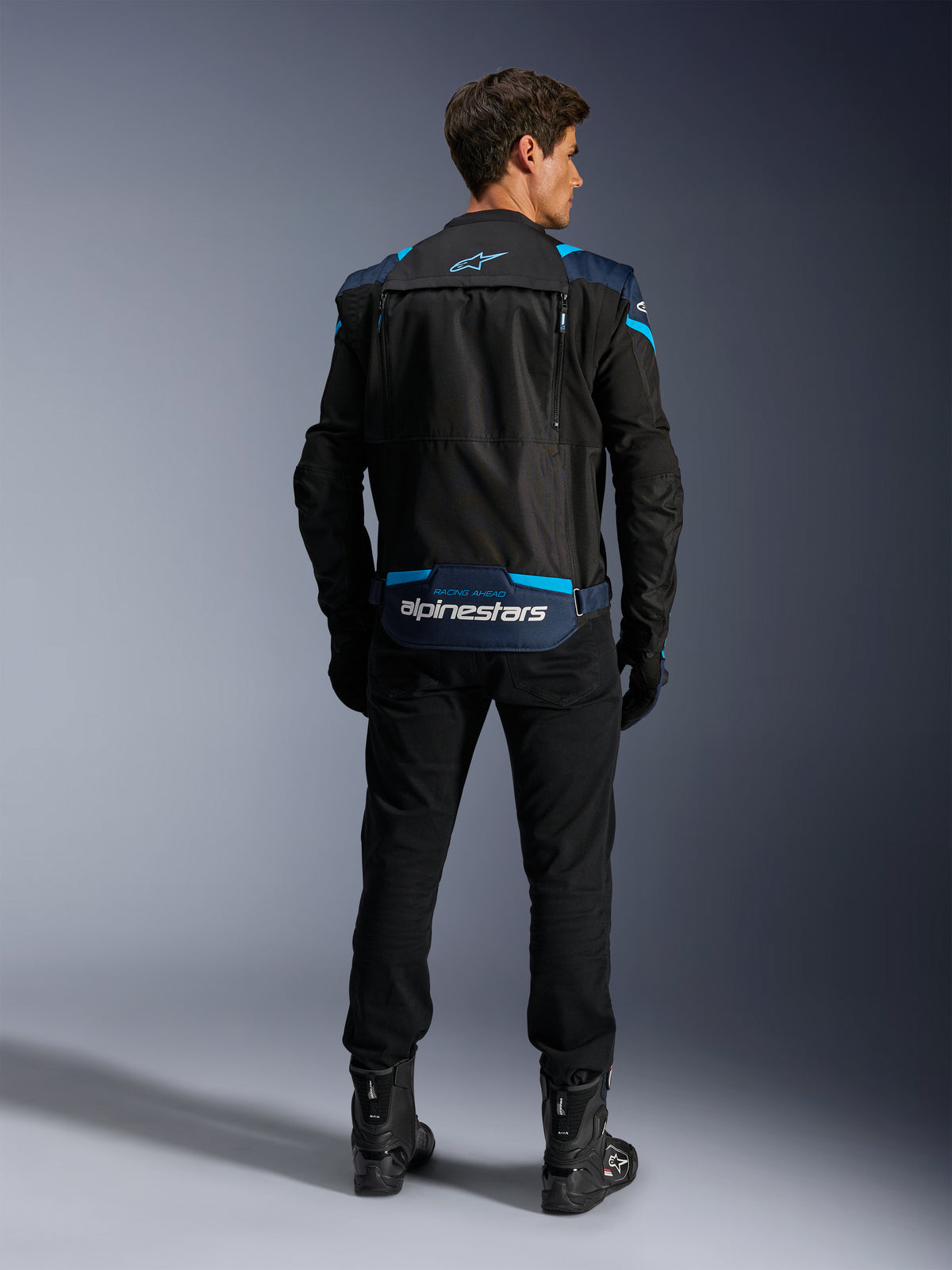 Alpinestars T-Stunt Air Jacket, Modular Textile Motorcycle Jacket, Black Dark Blue and Bright Blue, back view showing the lower back sleeve storage compartment with white Alpinestars branding, worn with black pants and boots.