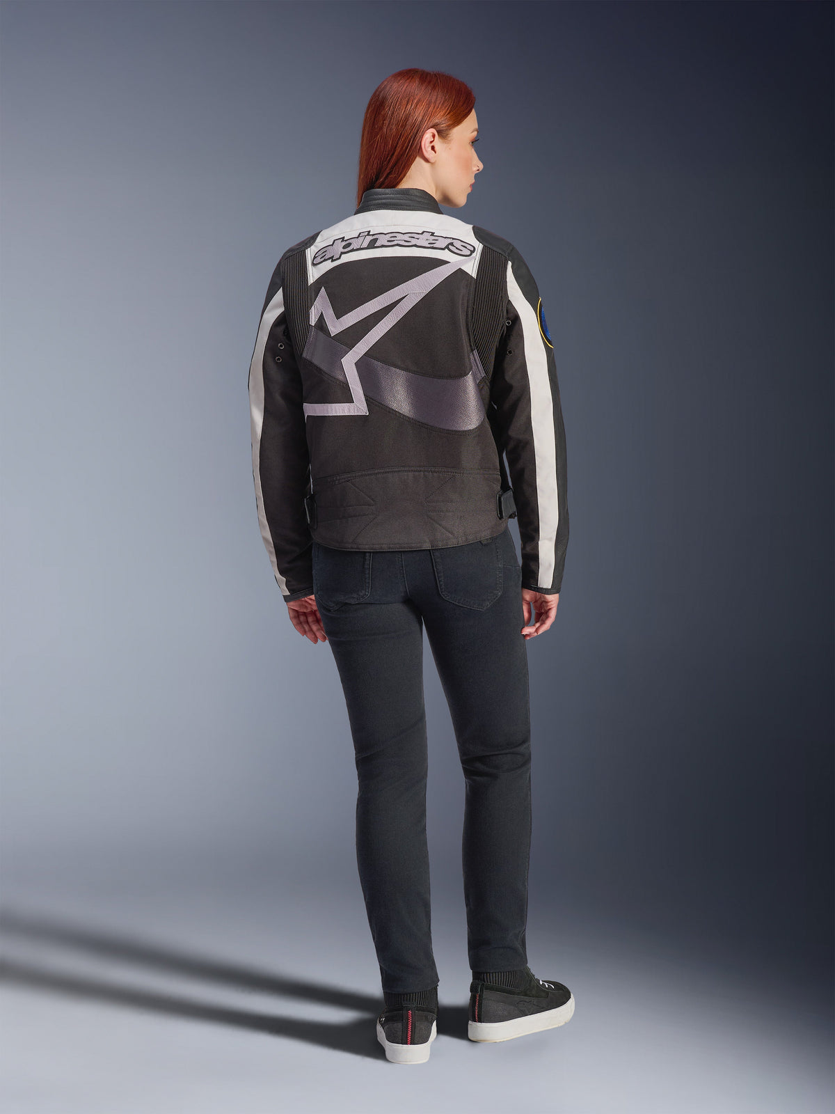 Alpinestars Idles Women’s Jacket, Urban Motorcycle Jacket, Black and Off-White, back view featuring a large grey Alpinestars logo and wordmark, worn with slim-fit black jeans and sneakers, vintage-inspired design for urban riding