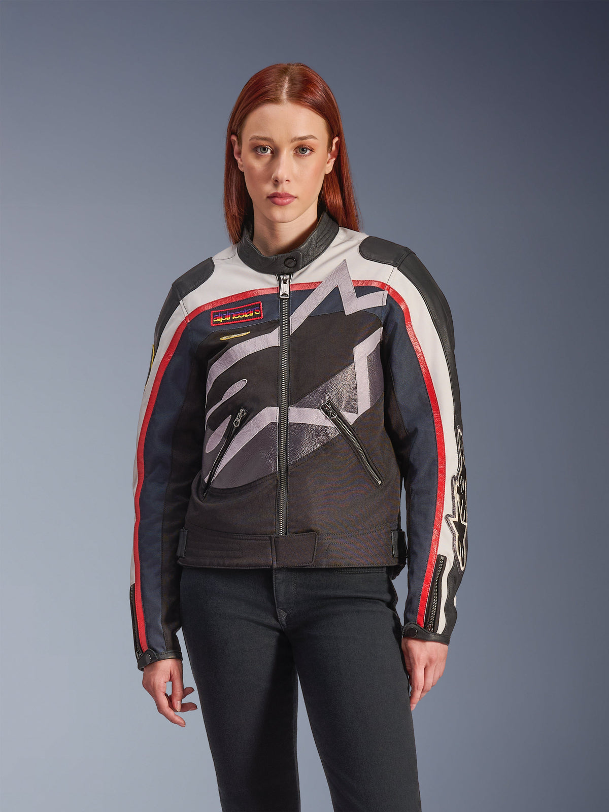 Alpinestars Idles Jacket, Women's Motorcycle Jacket, Off White Flame Red and Black, featuring a large stylized star logo, vintage-inspired chest patches, high biker collar, zippered pockets, and striped sleeves, worn by a female model with dark jeans.