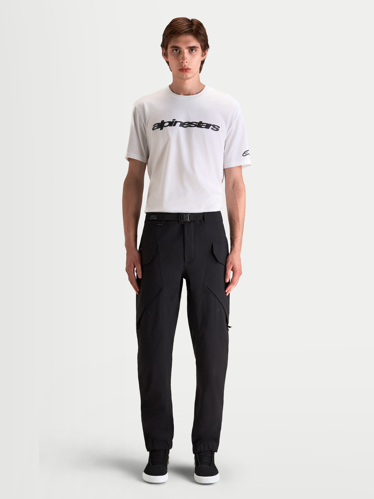 Alpinestars Juggernaut V2 Drystar® Pants, men's waterproof urban motorcycle pants in black, front view on a model wearing a white t-shirt and casual riding boots, showcasing utility cargo pockets and an adjustable belt waist.