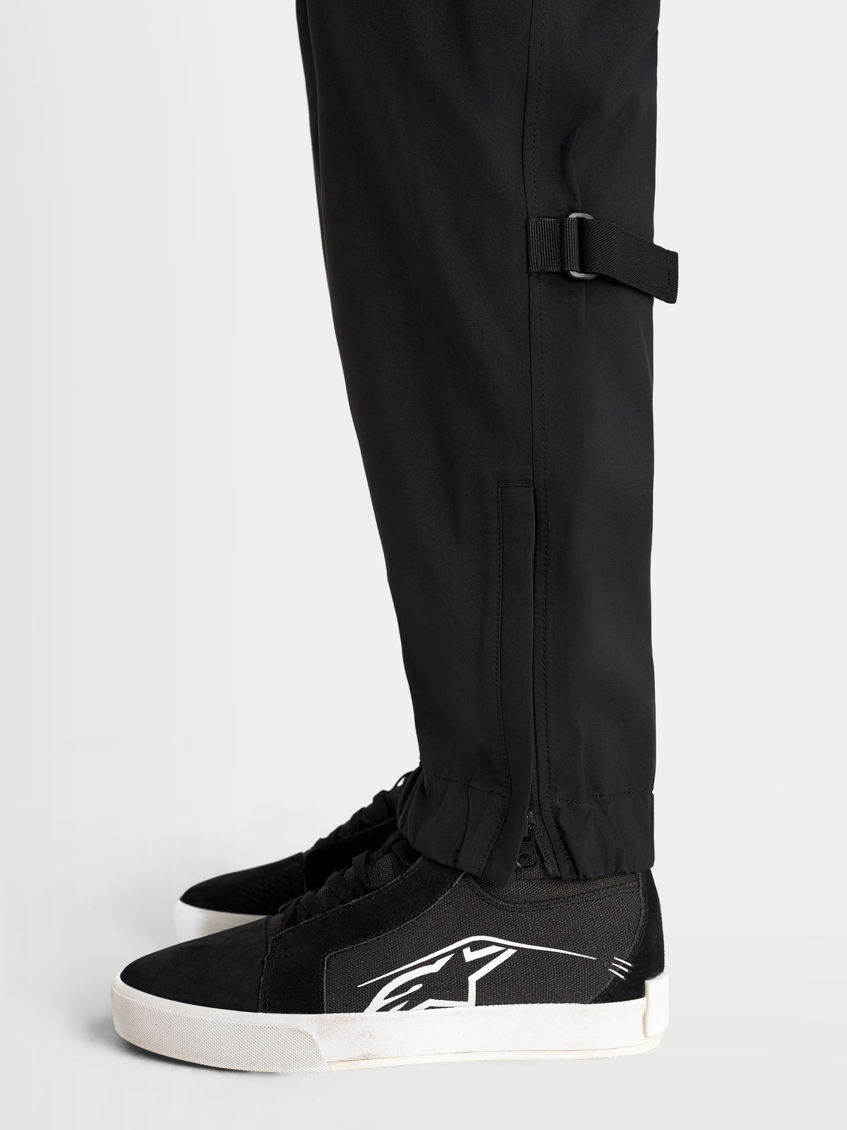 Alpinestars Juggernaut V2 Drystar Pants, urban contemporary motorcycle riding pants in black, close-up side view showing lower leg adjustment and elasticated hem with zippered opening