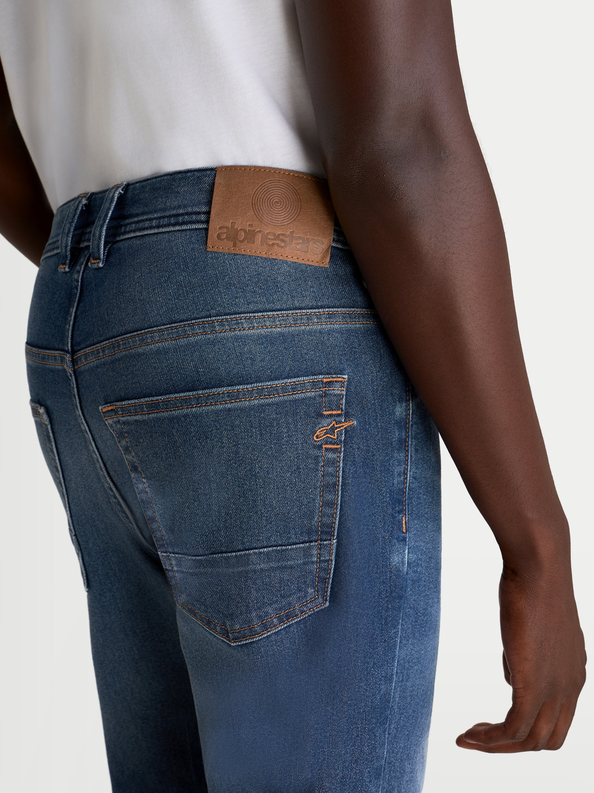 Alpinestars Flex-AST 8 Denim Pants Short, men's urban motorcycle jeans in medium blue, rear close-up view showing traditional five-pocket construction, branded leather waist patch, and topstitching details worn by a model
