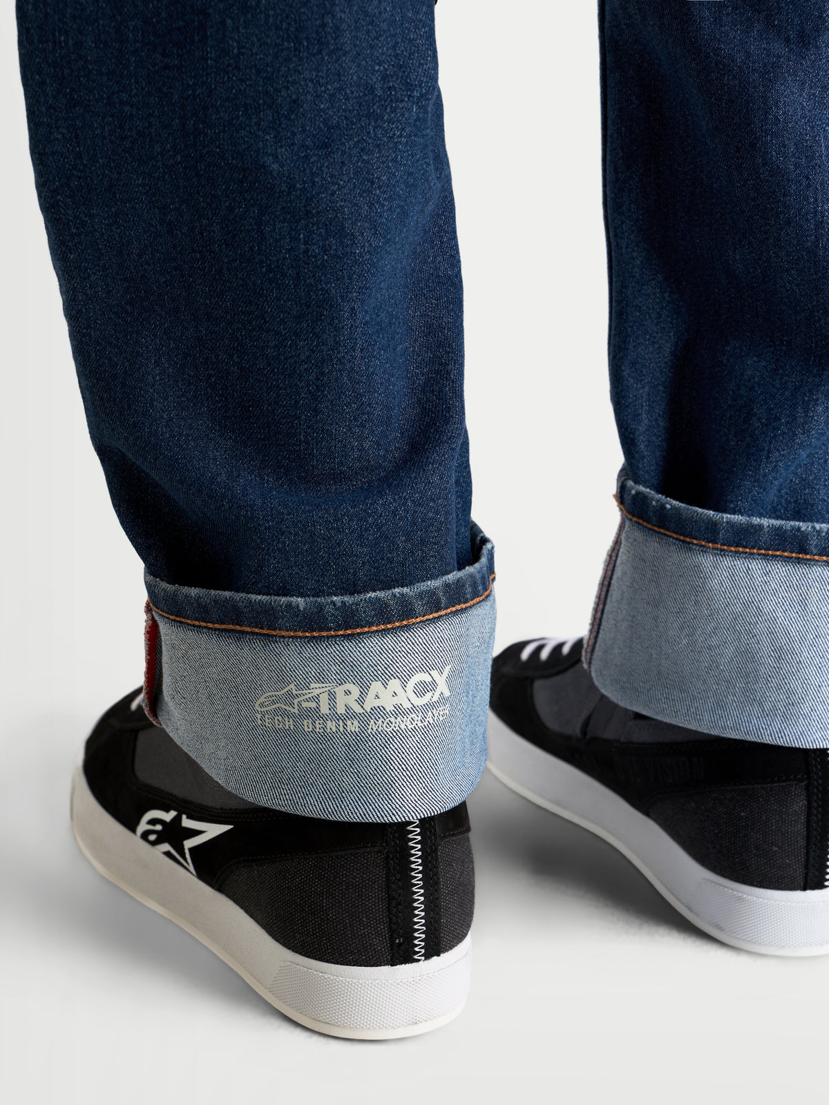 Alpinestars Flex-AST 8 Denim Pants, motorcycle denim pants in medium blue, close-up view of the cuffed hem showing the internal A-TRAACX single-layer technical denim branding and selvedge-style edge finish