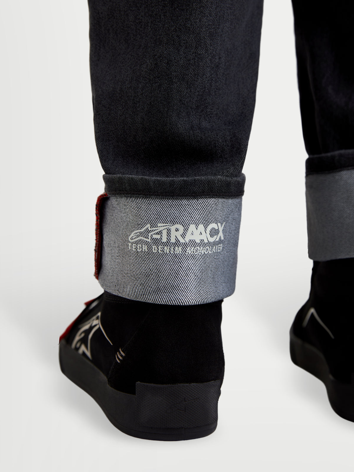 Alpinestars Flex-AST 7 Denim Pants Short, men's urban motorcycle riding jeans, faded black, detailed close-up showing cuffed hem with visible A-TRAACX technical denim branding and selvedge finish