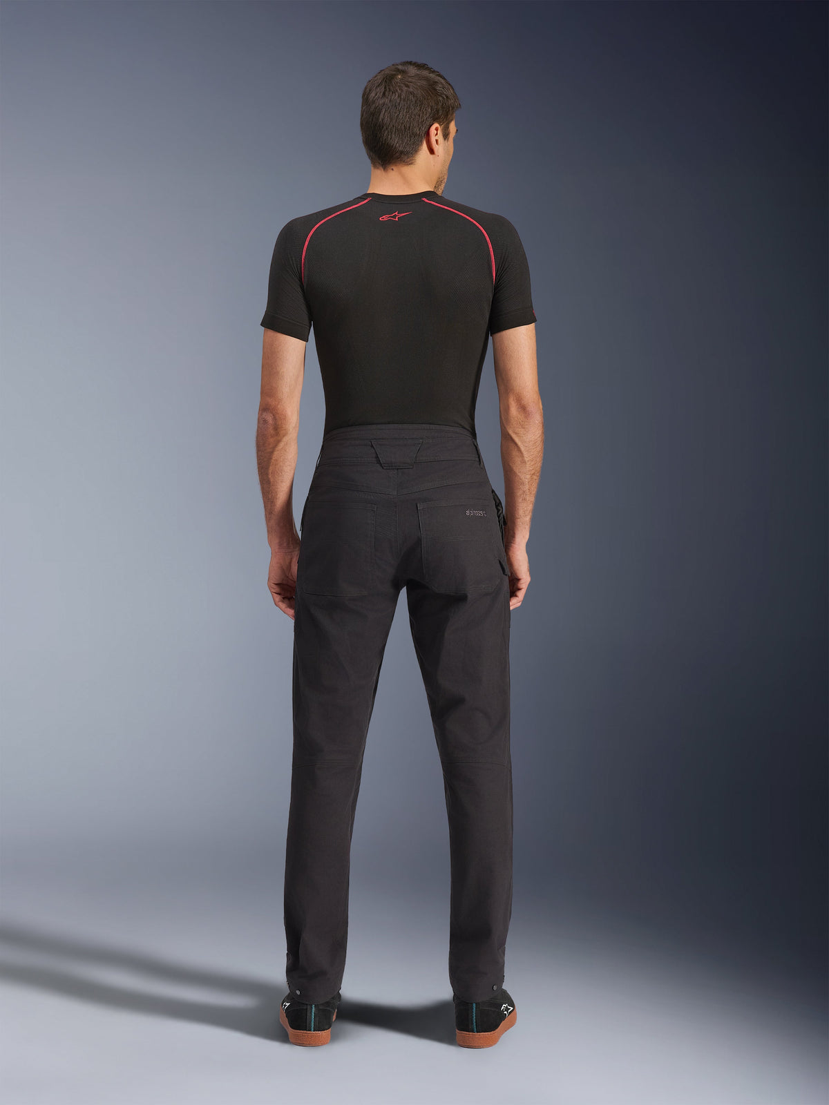 Alpinestars Flex-AST Canvas Pants, Urban Motorcycle Pants, Black, Rear view showing workwear-inspired design with back pockets and extended back rise, worn with a black base layer and sneakers, ergonomic ride fit