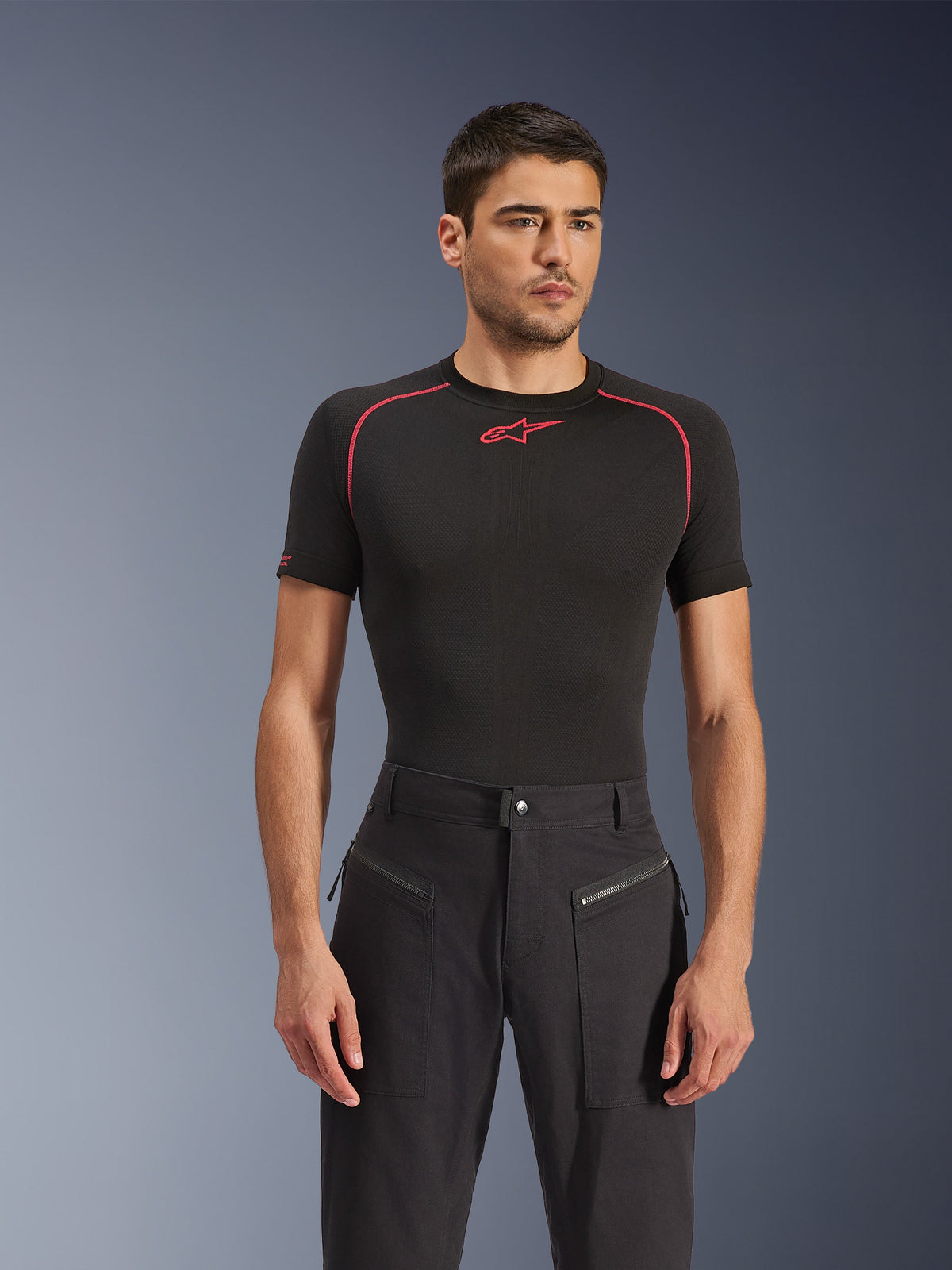 Male model wearing Alpinestars Flex-AST Canvas Pants in Black, urban motorcycle pants featuring visible zippered front pockets and a workwear-inspired design, paired with a black base layer with red accents.