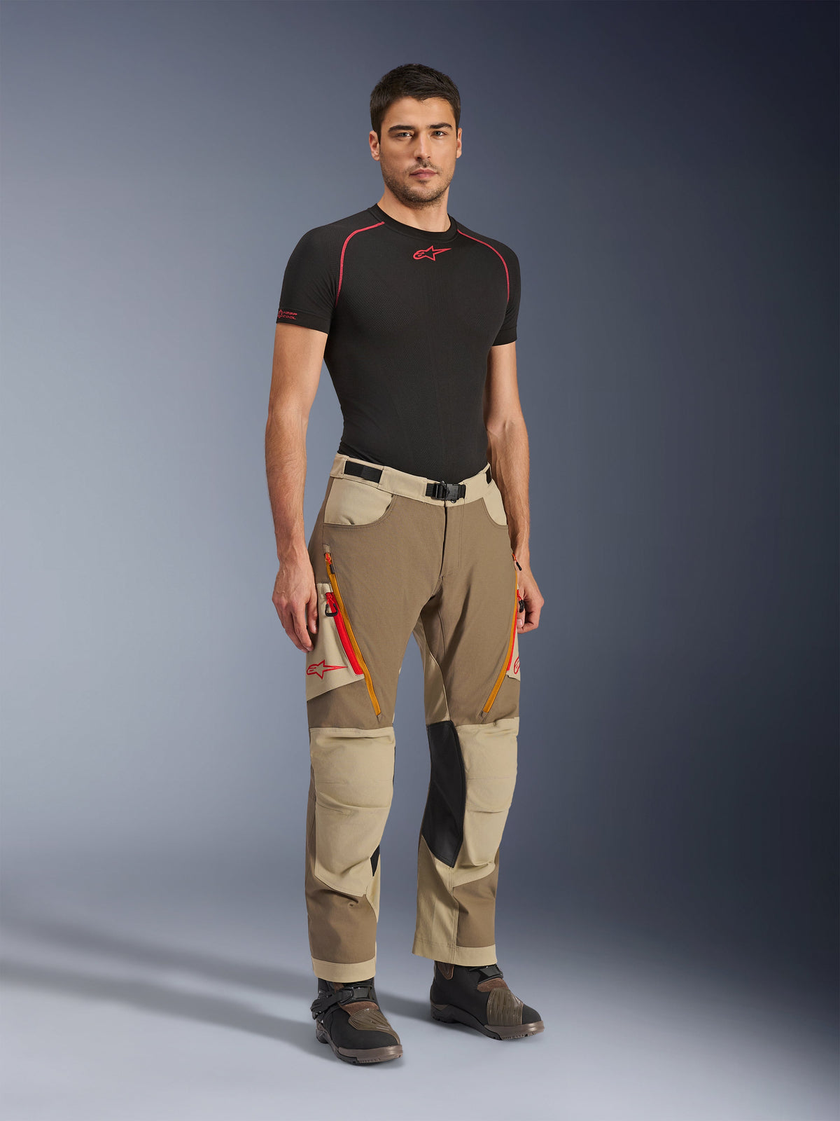 Alpinestars Maxdura Dual Pants in Walnut Aluminum, brown and tan adventure motorcycle pants with orange zippers and black leather knee panels, worn with a black base layer t-shirt and adventure boots, full-body front view