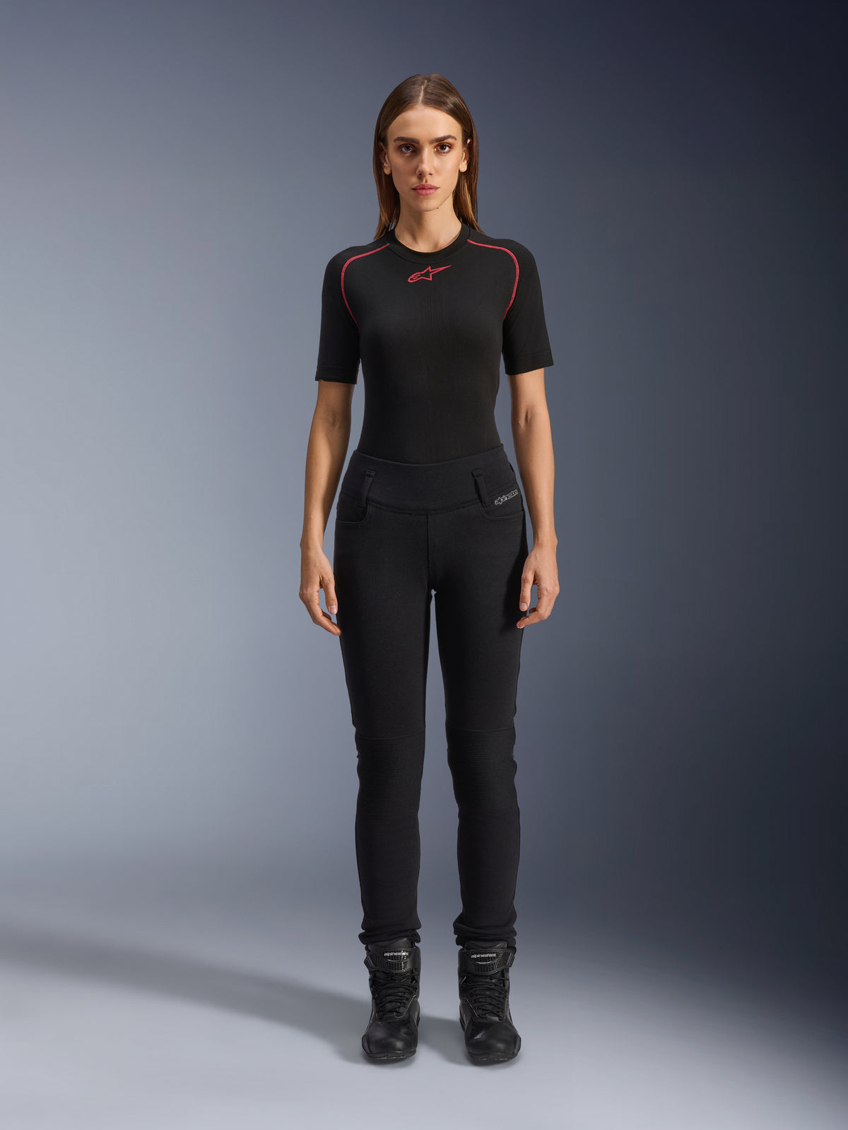 Alpinestars Womens Banshee Leggings, Black motorcycle leggings, figure-hugging anatomical fit, worn by a female model with a black base layer and motorcycle boots, featuring ribbed knee panels and high-waisted construction for urban riding.