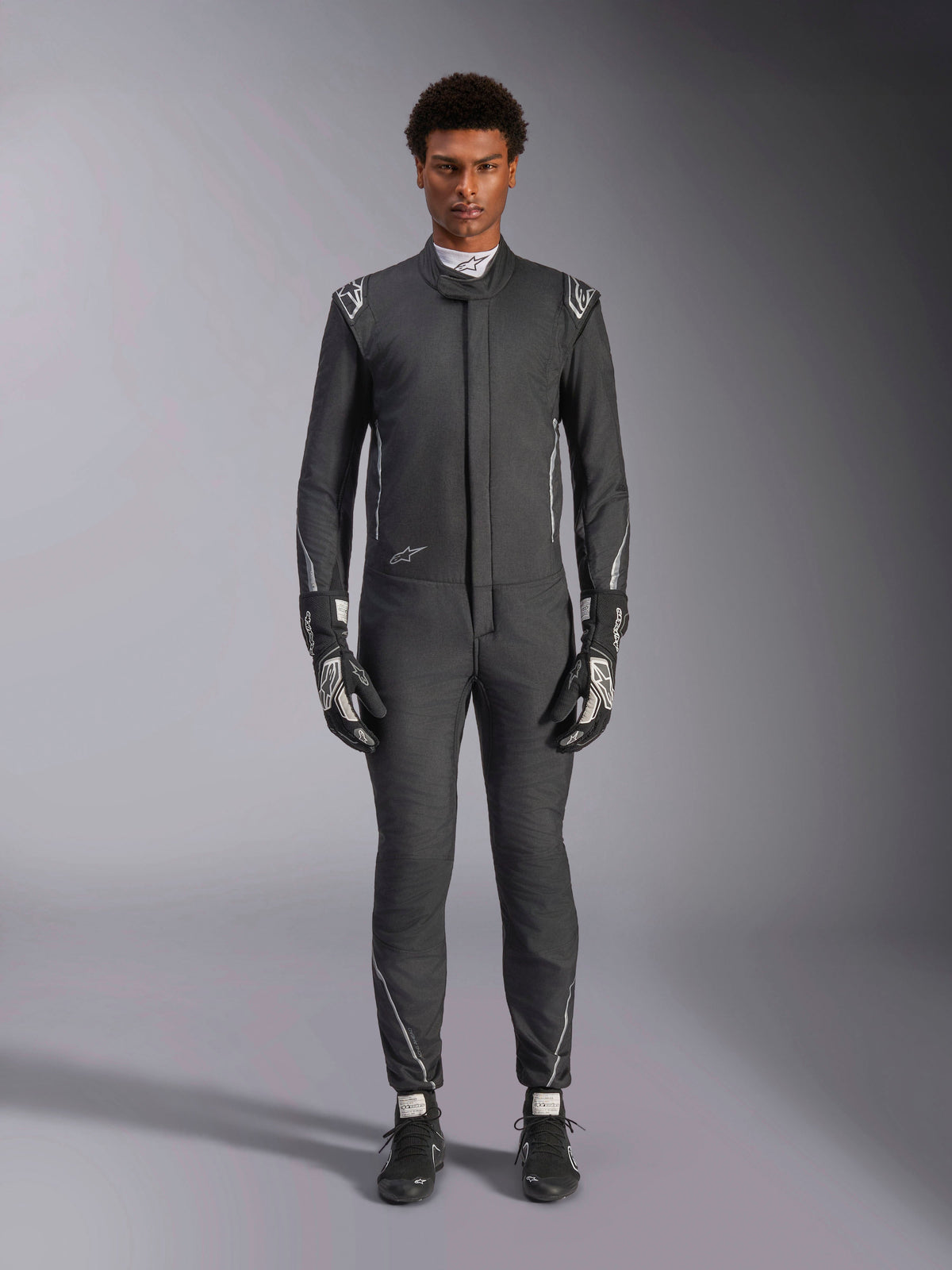 Alpinestars Hypertech V3 Suit, professional auto racing suit, Black and Dark Shadow, worn by a model with matching racing gloves and shoes, slim athletic fit with silver accents and branding, performance motorsport gear