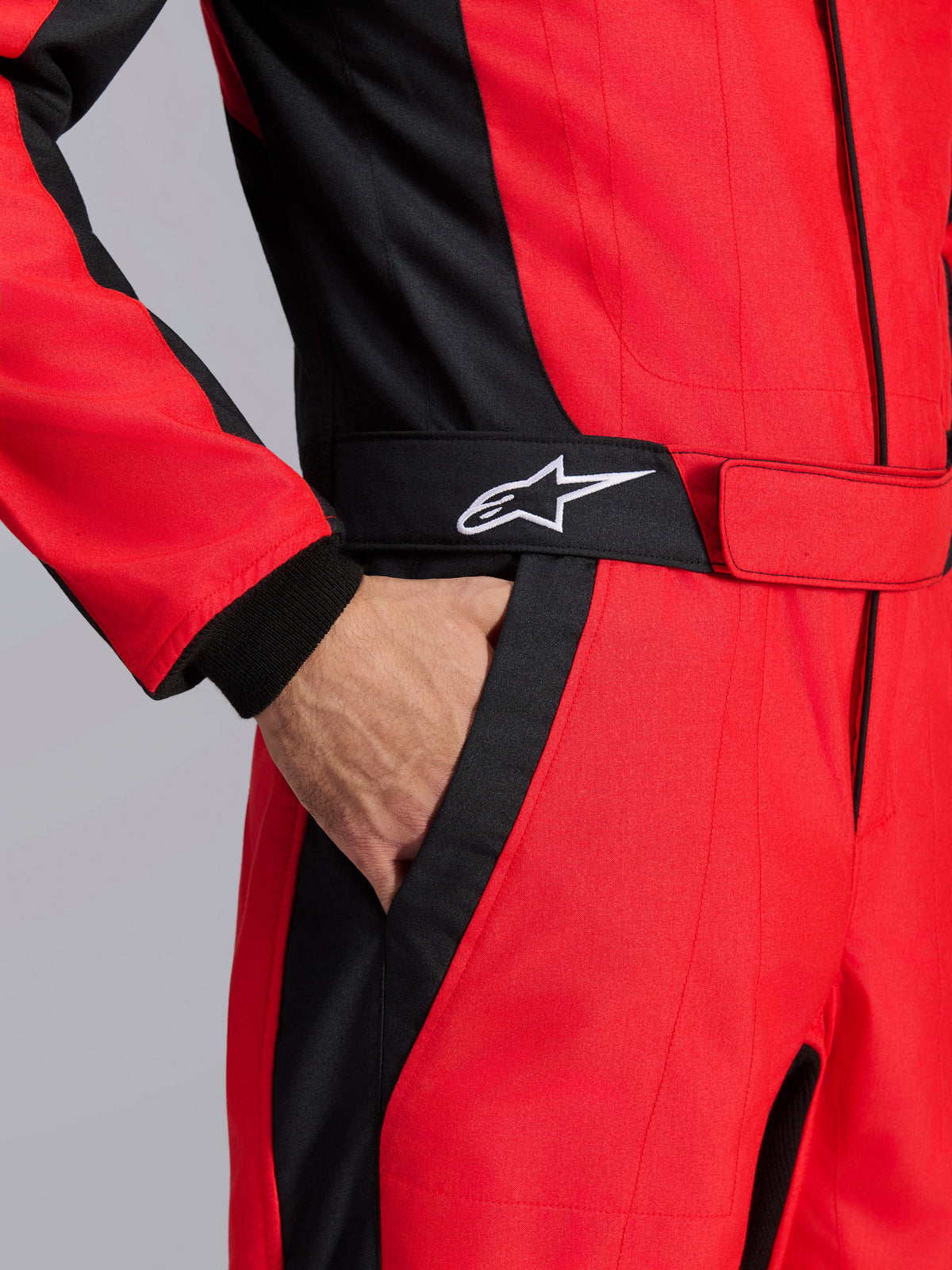 Alpinestars GP Pro Comp V2 FIA Racing Suit, Red and Black, close-up of the waist area showing a hand in the pocket, featuring a black belt with a white star logo and structured panels for auto racing