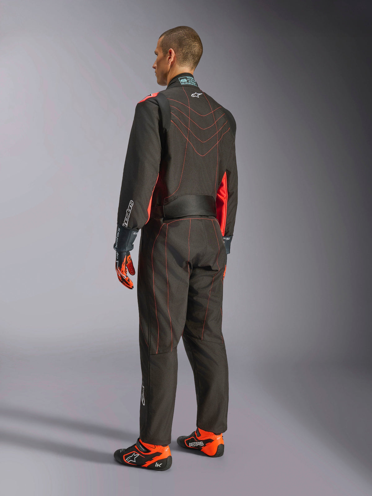 Alpinestars KMX-9 V3 Suit, Karting Race Suit, Black and Red Fluo, back view, featuring red contrast stitching and fluorescent side panels, worn with racing gloves and karting shoes, professional motorsport apparel