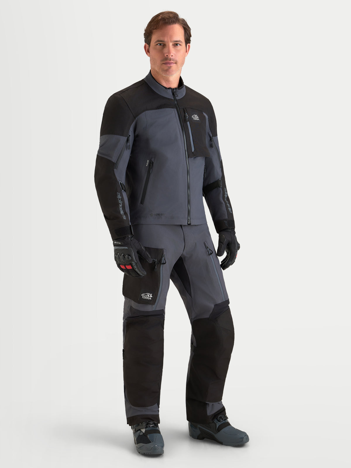 Alpinestars Arenis Gore-Tex Jacket, men's all-terrain adventure touring motorcycle jacket in black and deep gray, worn with matching riding gear, waterproof textile construction.