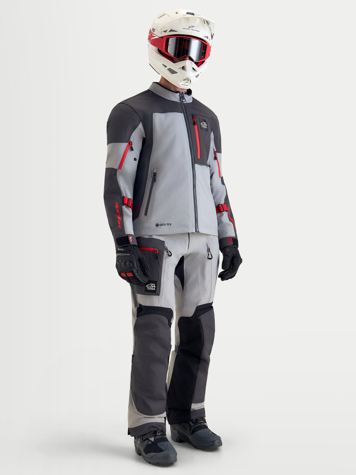 Alpinestars Arenis Gore-Tex® Jacket, men's adventure touring motorcycle jacket in mid gray, deep gray, and black with red accents, full gear setup with matching pants, helmet, and goggles on model.