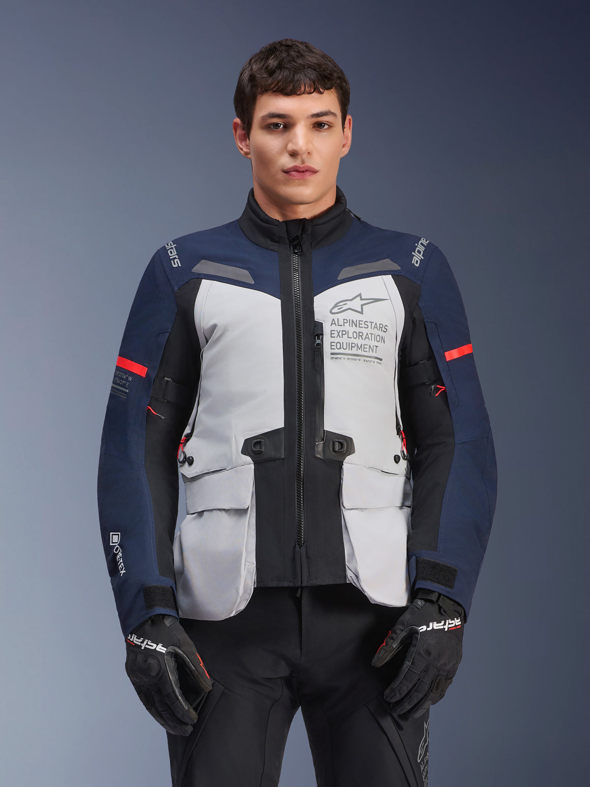 Alpinestars ST-7 2L GORE-TEX Jacket, Motorcycle Adventure Touring Jacket, Ice Gray and Dark Blue with Red accents, Waterproof and breathable, worn by a model with black gloves, featuring Alpinestars Exploration Equipment branding on the chest