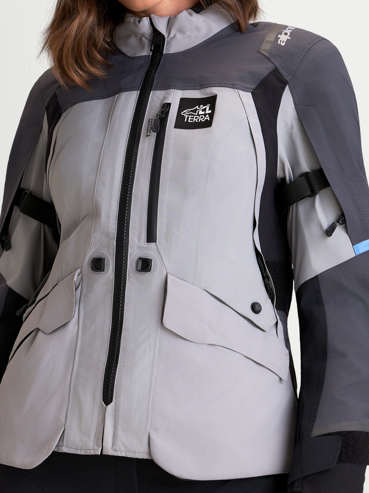 Alpinestars Stella ST-7 V2 2L GORE-TEX Jacket, women's adventure touring motorcycle jacket in mid gray, deep gray, and black, close-up view showing waterproof textile construction, front pockets, and All Terra logo badge worn by a model.