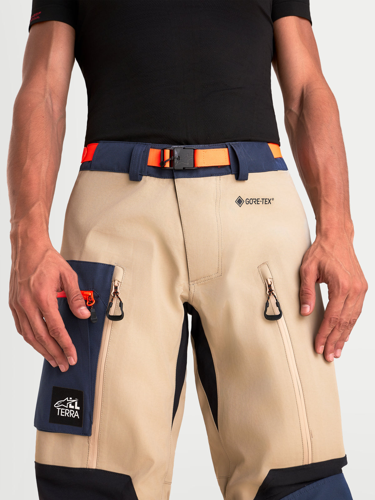 Alpinestars Arenis Gore-Tex Pants, men's adventure touring motorcycle pants in aluminum, night navy, and orange, close-up view of the waist, magnetic buckle belt, GORE-TEX logo, zippered thigh vents, and cargo pocket worn by a model.