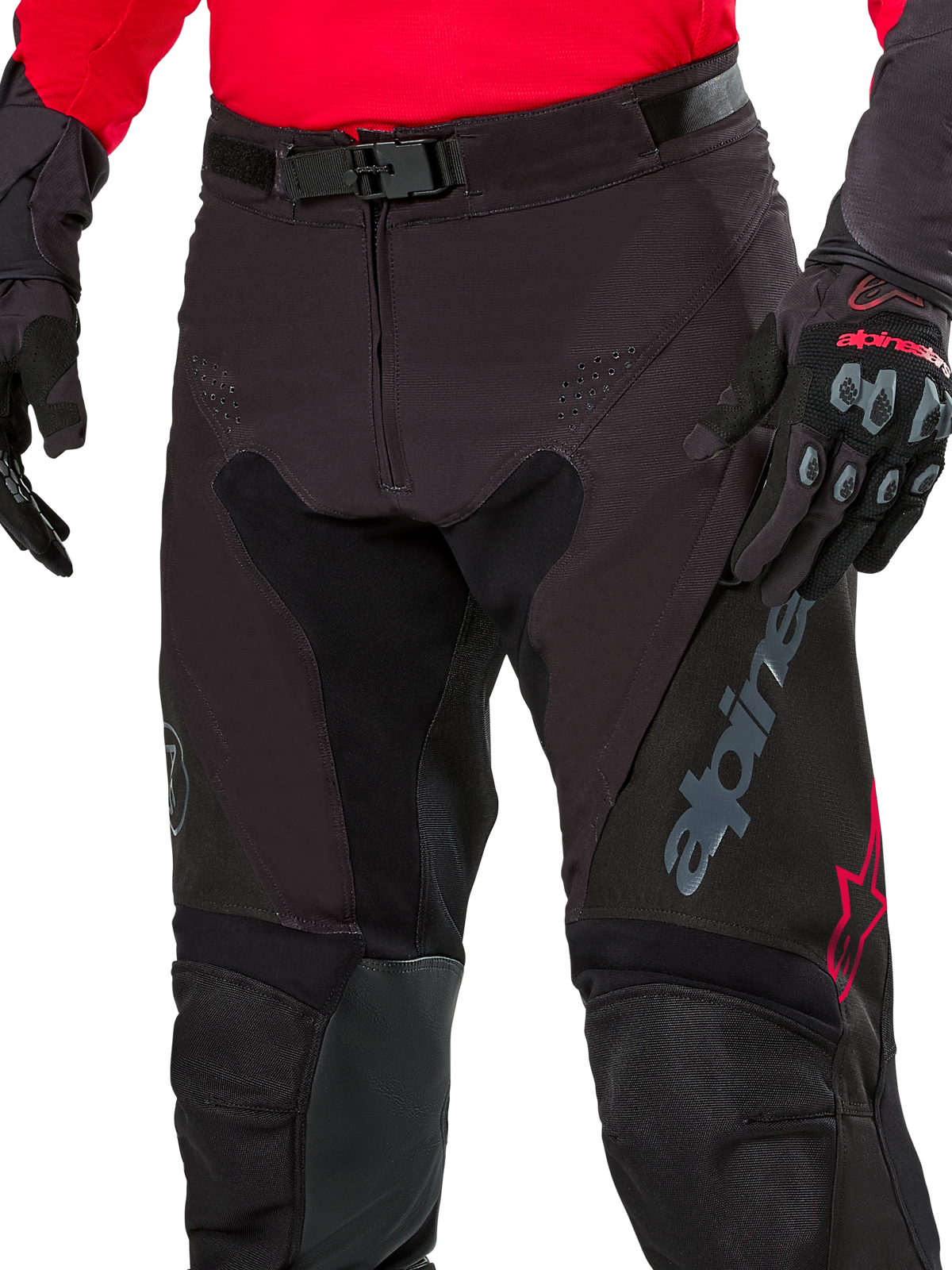 Close-up of Alpinestars Pro-Dura Pants, Enduro Pants, Black Magnet White with red accents, featuring a secure magnetic buckle closure and zip fly, worn with matching red jersey and black gloves, durable ripstop construction for off-road riding