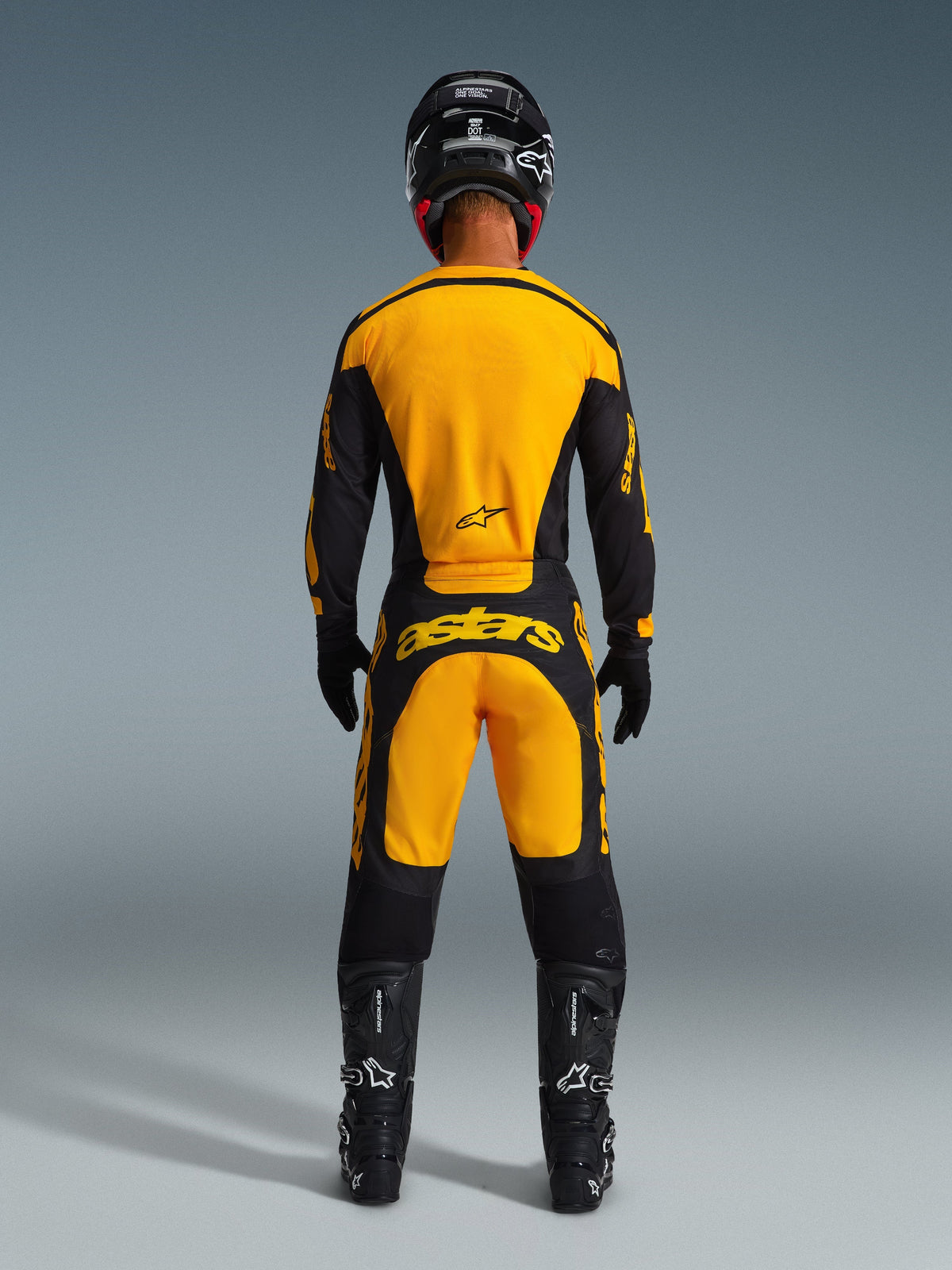Motocross rider from behind wearing Alpinestars 2026 Racer Riway Pants and matching jersey in Yellow and Black, featuring bold yellow branding on the back, paired with a black helmet, black gloves, and black motocross boots, complete off-road racing gear set