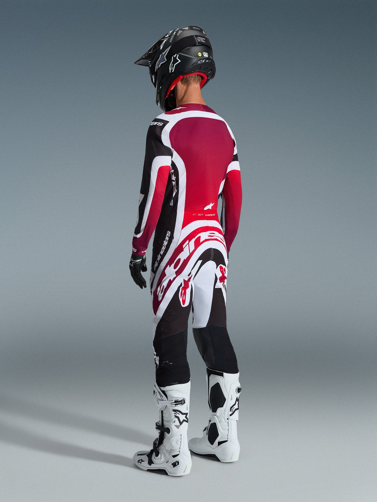 Motocross rider from behind wearing Alpinestars 2026 Supertech AFD Vista Pants, Black Red and White, matching jersey, black helmet, and white and black boots, full-body rear view of professional racing gear