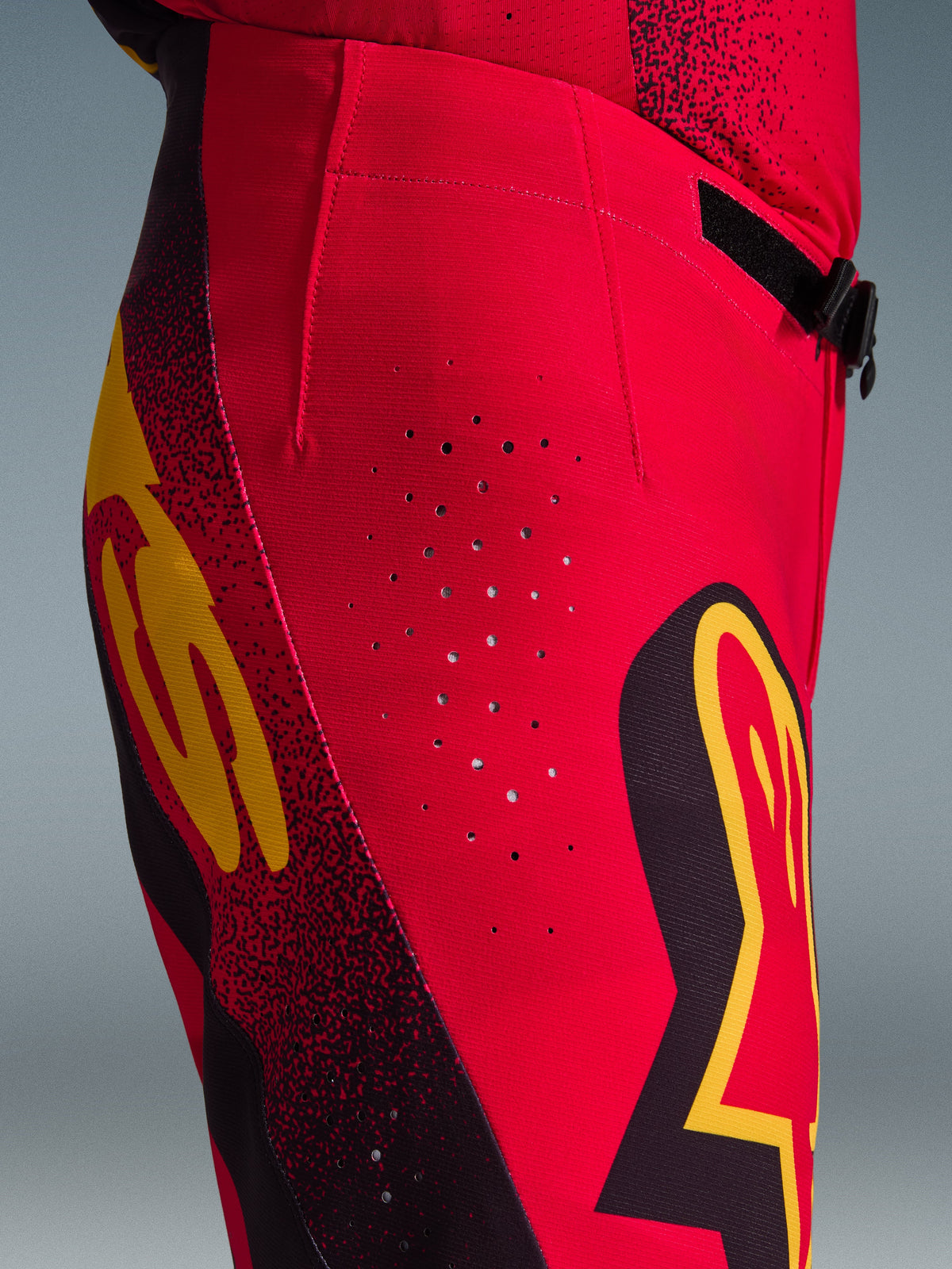 Alpinestars 2026 Supertech Scenz Pants, Motocross Pants, Red Black and Yellow, close-up side view featuring laser-cut ventilation perforations, bold graphic logos, and high-performance stretch rip-stop fabric for motocross racing.