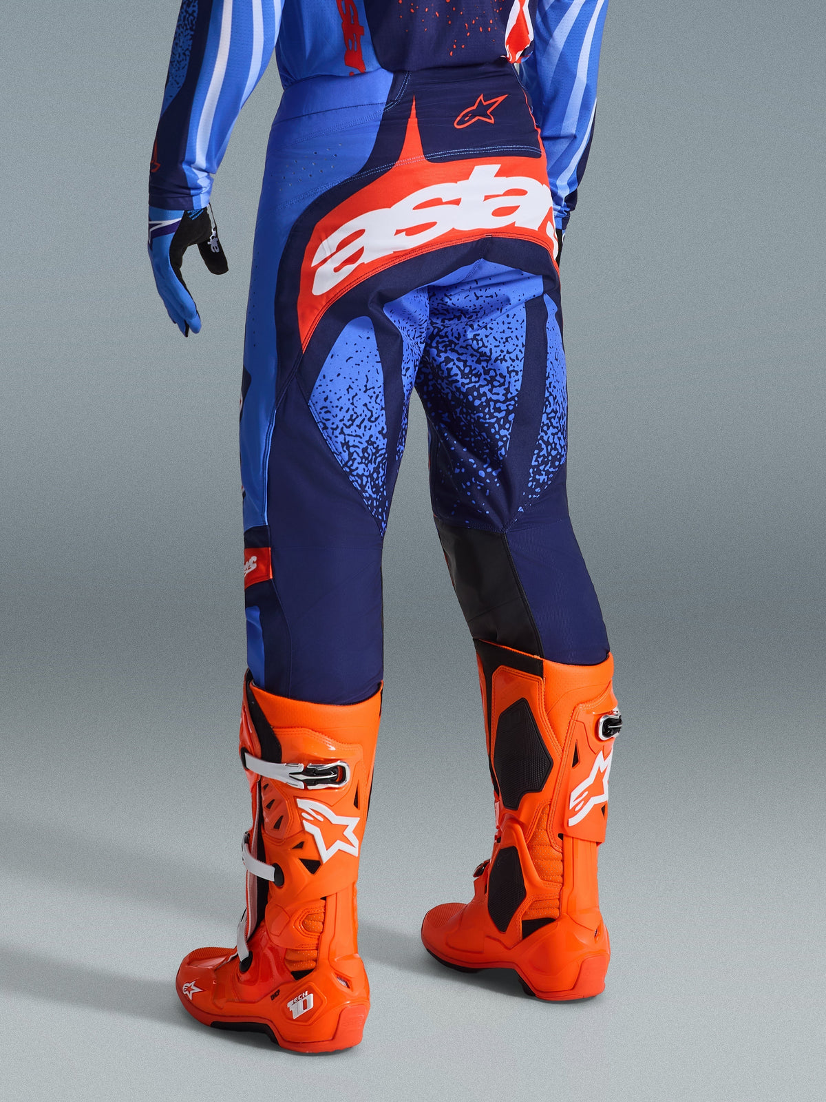 Alpinestars 2026 Techstar Nomur Pants, Motocross Pants, Dark Navy, Orange, and UCLA Blue, rear view showing white 'Astars' logo on the seat, worn with bright orange motocross boots and matching jersey, athletic race fit for off-road competition.