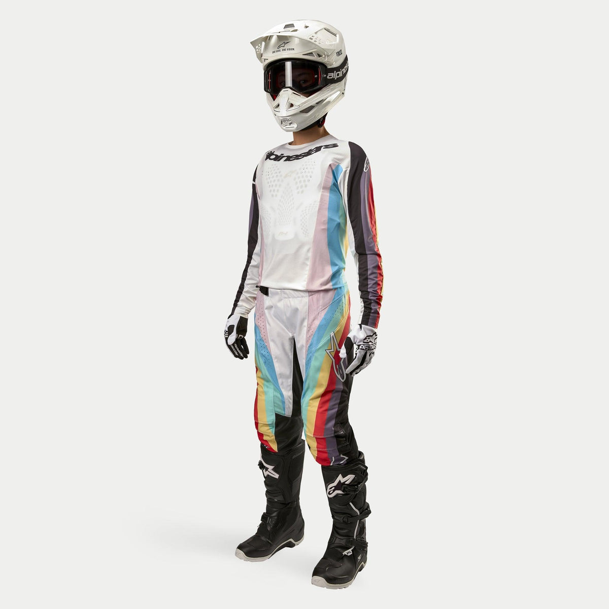 Motocross rider wearing Alpinestars Women Stella 2024 Techstar Pants, Motocross Pants, Black Multicolor featuring white panels and vibrant diagonal stripes, matching jersey, white helmet, and black boots, coordinated off-road racing outfit for women