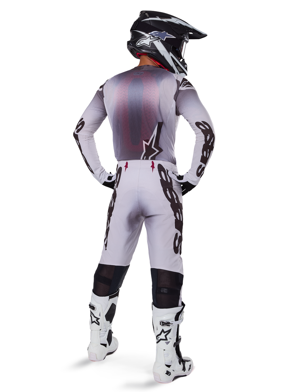 Motocross rider wearing complete racing gear, grey and black jersey, light grey pants with black 'Astars' branding on the sides, black and white helmet, White Tech 10 Boots, coordinated professional off-road racing outfit