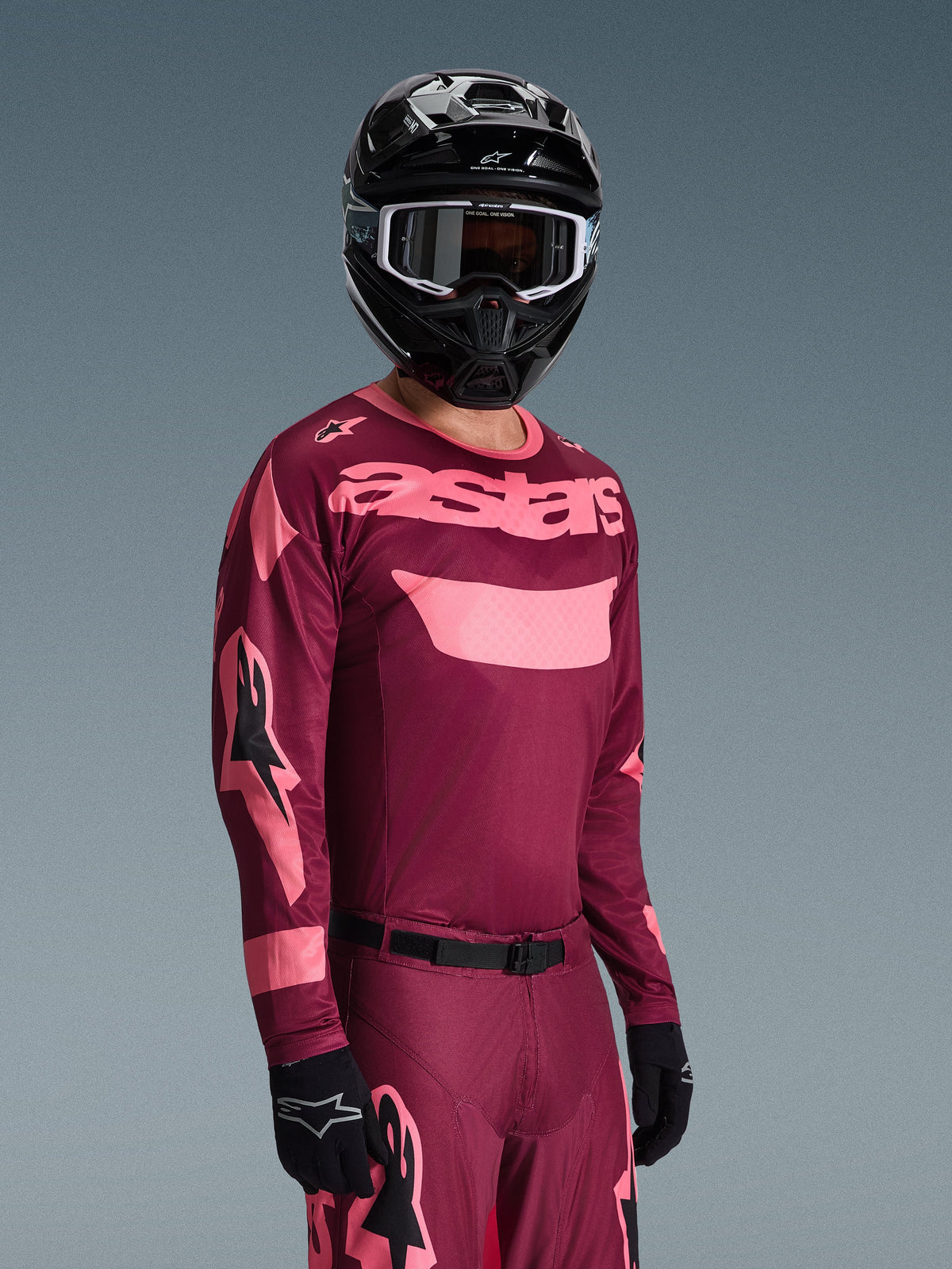Motocross rider wearing Alpinestars 2026 Racer Riway Gear Set, Burgundy and Pink jersey with bold 'astars' branding, matching pants with pink accents, black helmet and gloves, professional racing outfit for off-road motocross