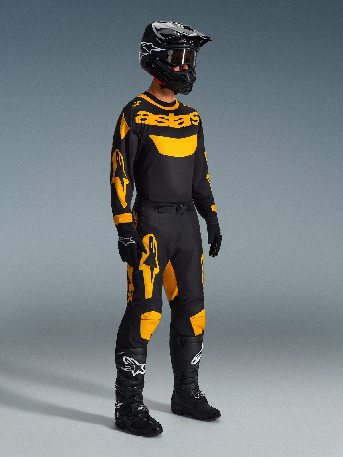 Motocross rider wearing complete racing gear, Alpinestars 2026 Racer Riway Jersey in Yellow and Black, matching black and yellow pants, black helmet with goggles, black boots, and gloves, coordinated outfit for off-road racing