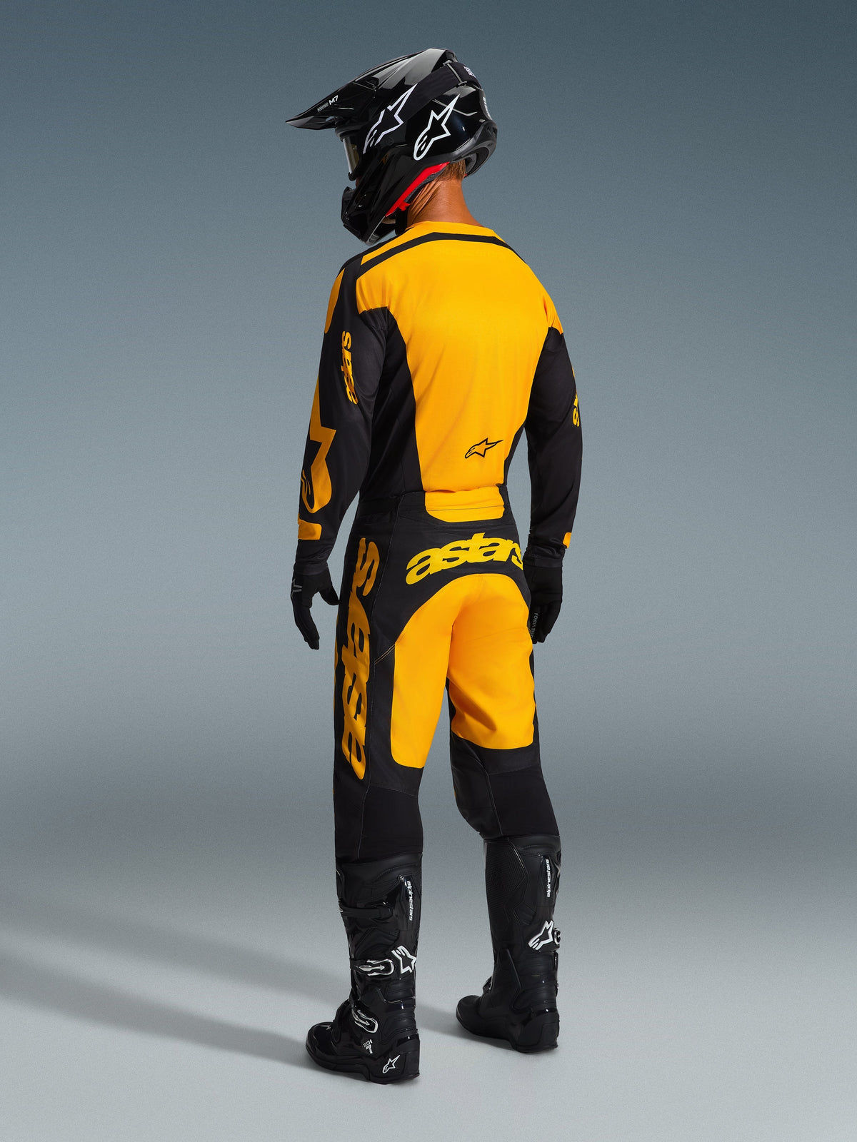 Motocross rider from behind wearing the Alpinestars 2026 Racer Riway Gear Set, Yellow and Black jersey and matching pants, black helmet, black gloves, and black boots with white accents, coordinated outfit for professional off-road racing.