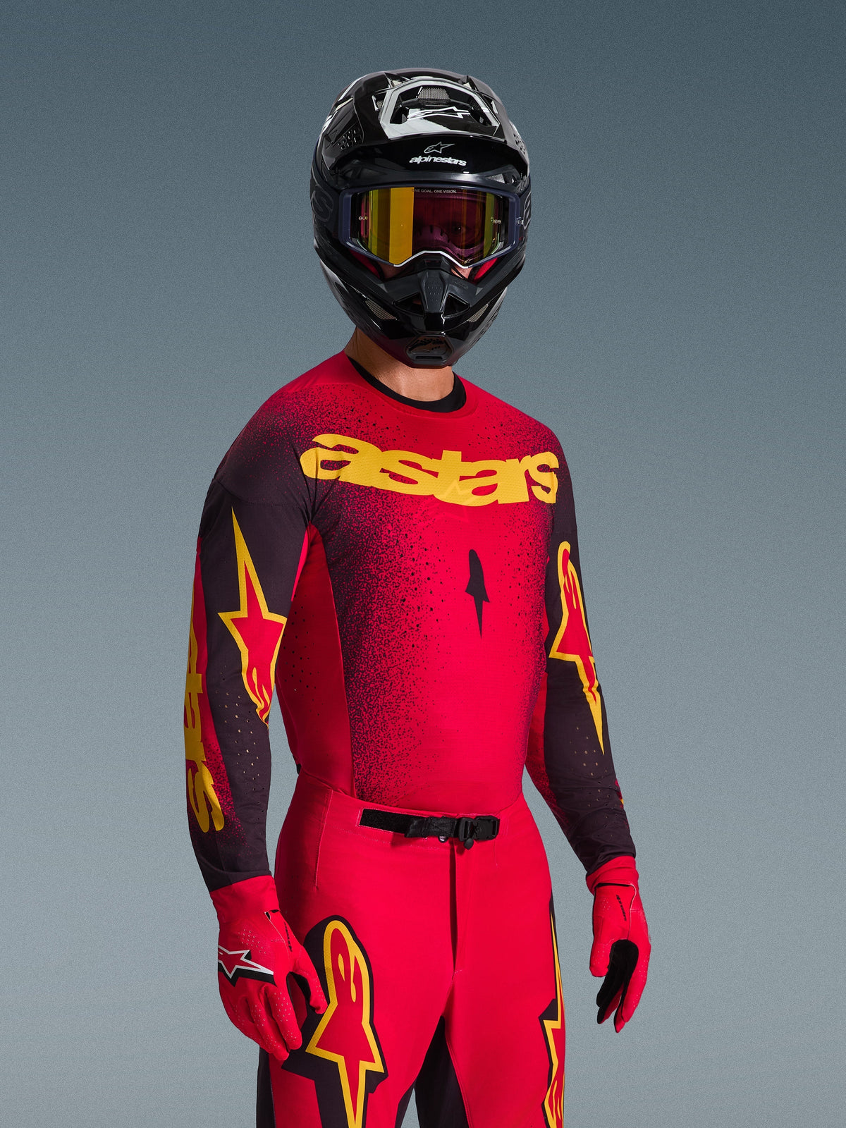 Motocross rider wearing Alpinestars 2026 Supertech Scenz Gear Set, Red and black jersey with yellow 'astars' logo and stipple gradient, matching red pants, red gloves, and a black helmet with yellow goggles, professional racing gear for motocross
