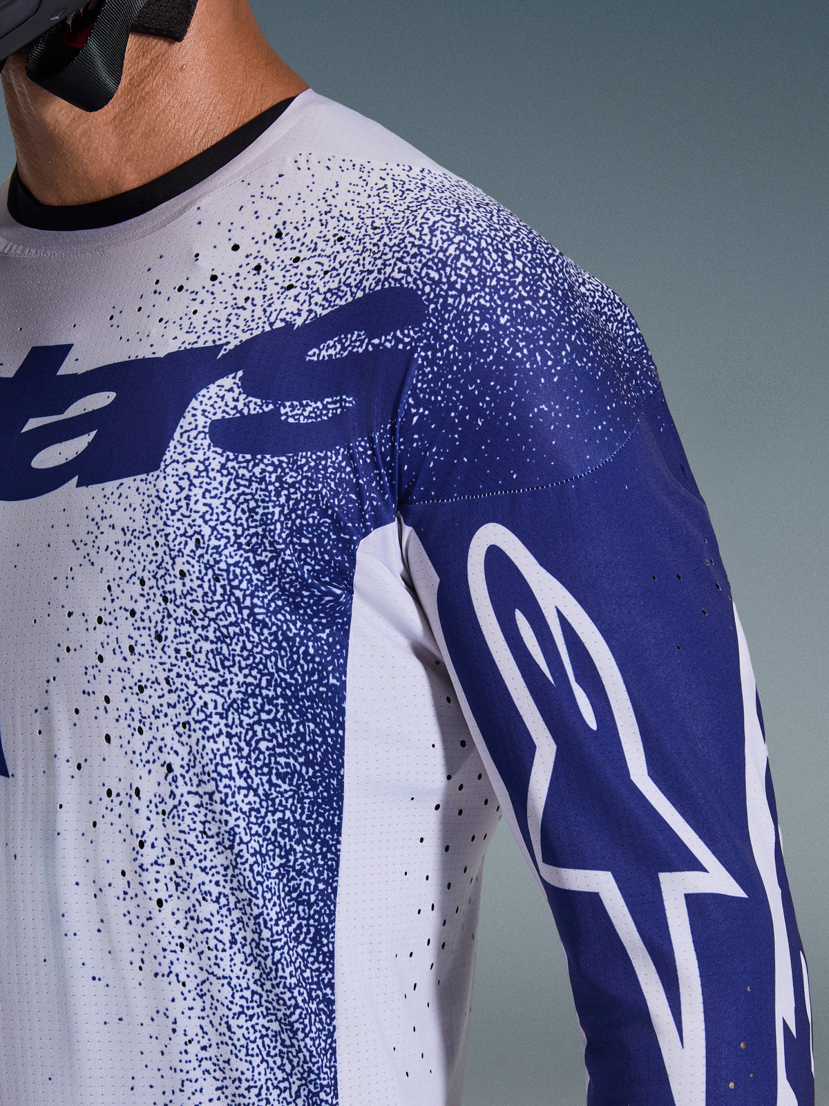 Close-up of the Alpinestars 2026 Supertech Scenz Jersey in Light Gray and Dark Blue, featuring laser-cut perforations, speckled graphic pattern, white Astars logo on the sleeve, professional motocross performance fit