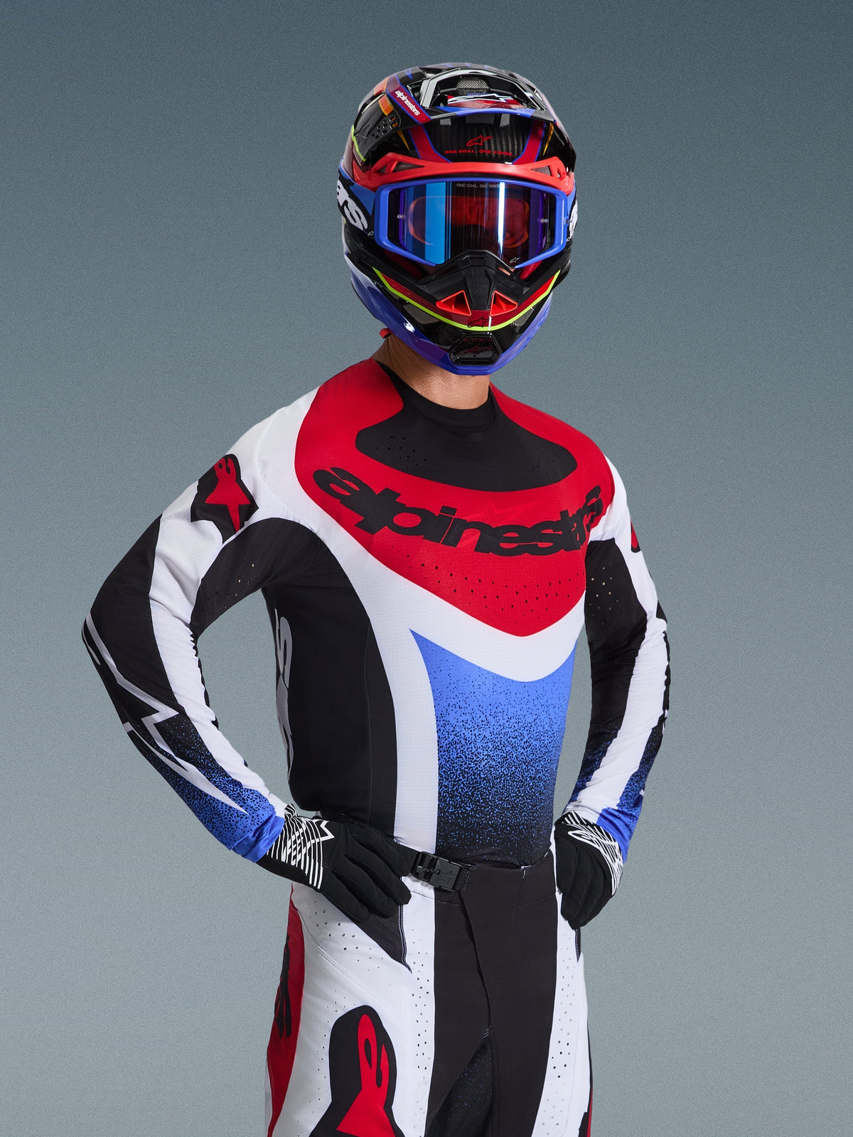 Motocross rider wearing the Alpinestars 2026 Techstar Knif Jersey in Red White and Blue, featuring black branding on the chest, paired with matching motocross pants, a coordinated racing helmet with blue goggles, and black and white gloves, professional off-road gear for competition