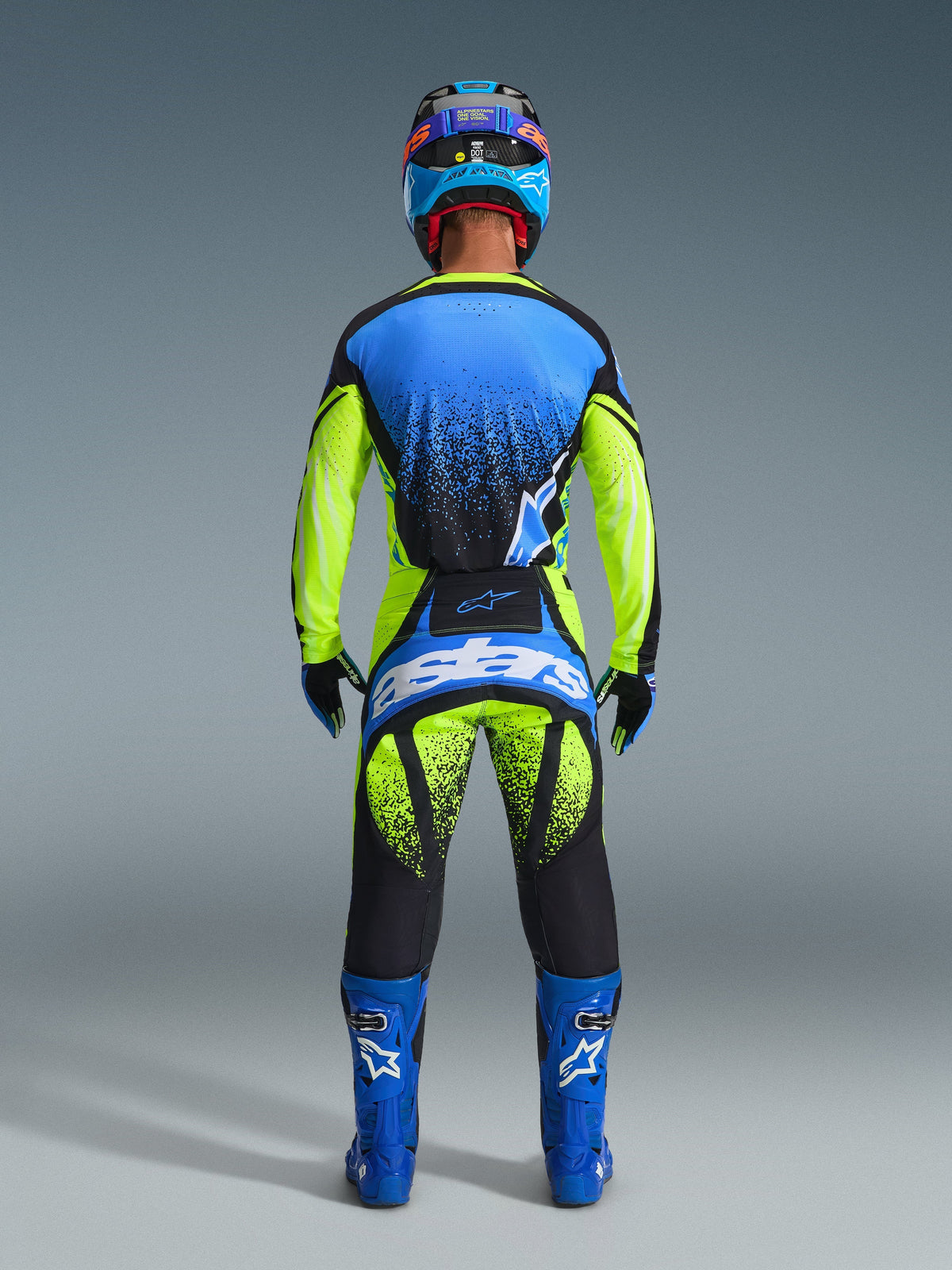 Rear view of a motocross rider wearing the 2026 Techstar Nomur Jersey in Dark Navy, Yellow Fluo, and UCLA Blue, paired with matching yellow and black motocross pants featuring 'Astars' branding, blue racing boots, and a coordinated helmet, complete professional gear for off-road racing.