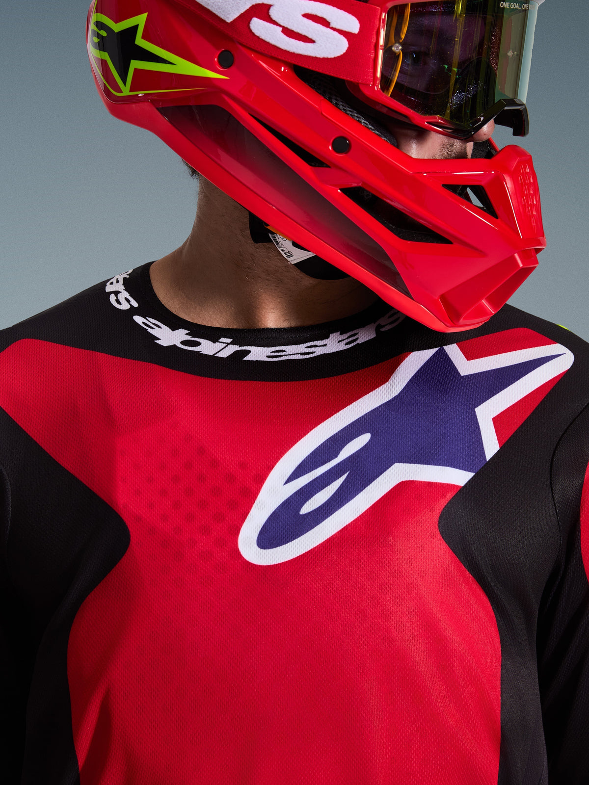 Alpinestars 2026 Fluid Grid Jersey, Red Black Purple, motocross rider wearing the jersey with a matching red helmet and goggles, large white and purple logo on the chest, sport collar with Alpinestars branding, technical off-road racing gear