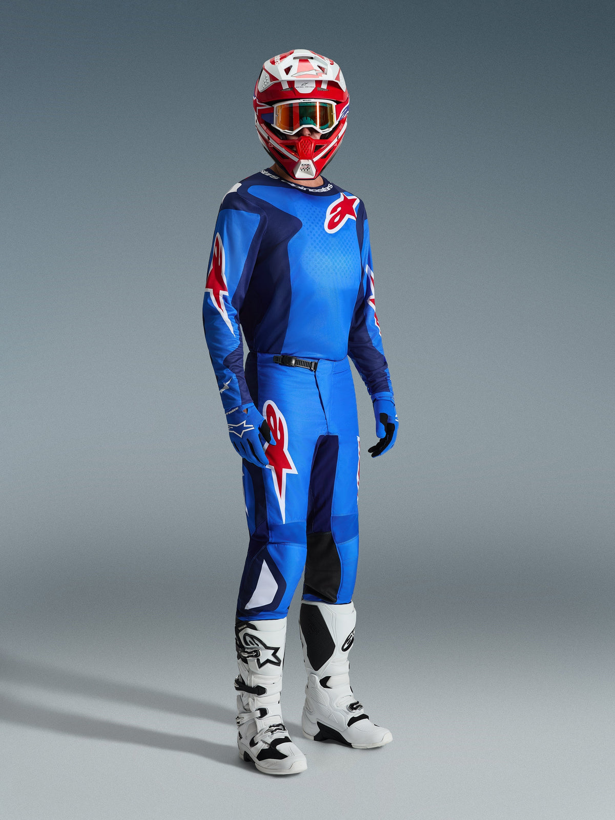 Motocross rider wearing the Alpinestars 2026 Fluid Grid Jersey in Blue Red, paired with matching motocross pants, white and black boots, and a red and white helmet, professional gear set for off-road performance.