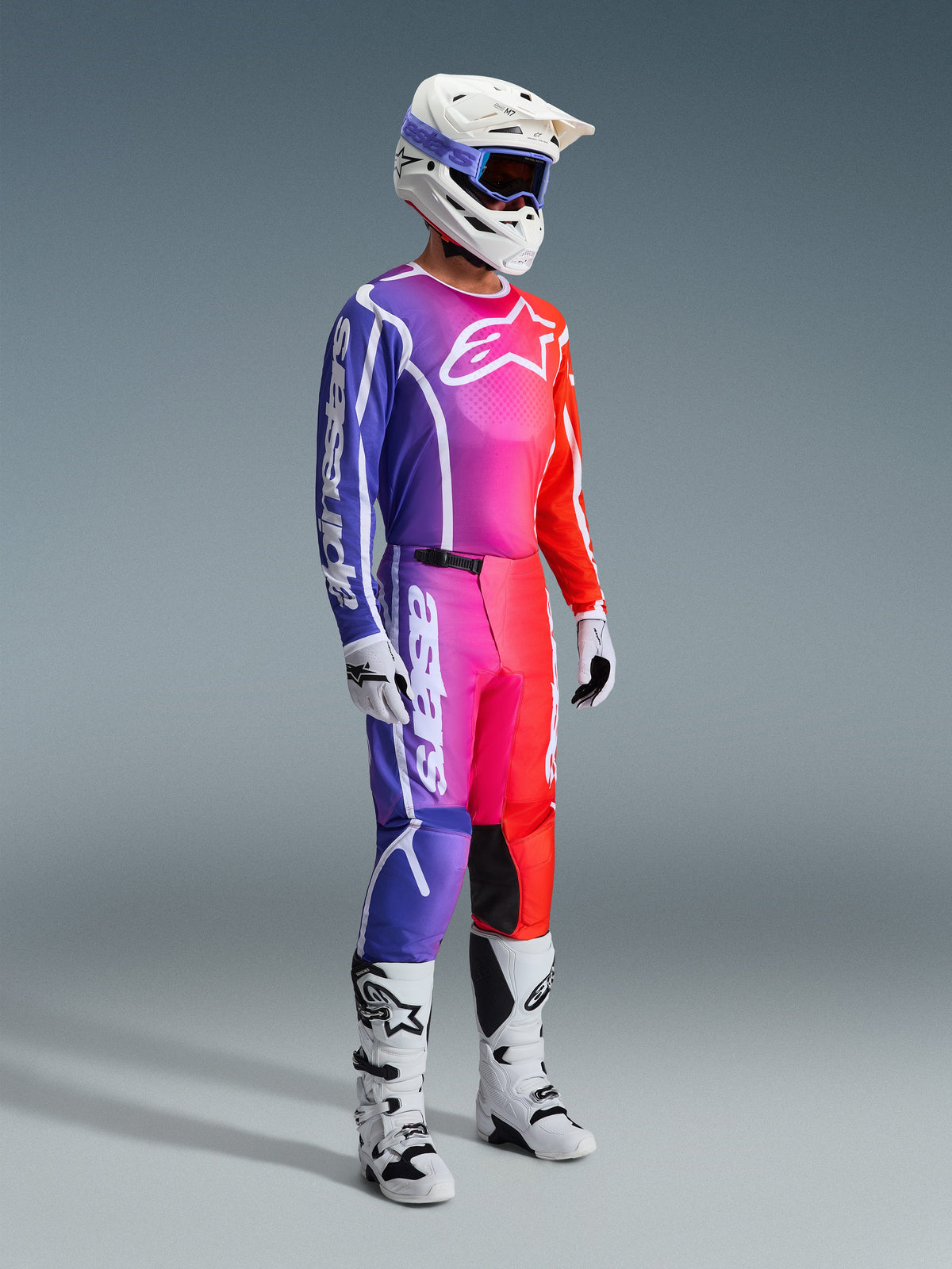Alpinestars 2026 Fluid Apex Gear Set, Motocross rider wearing a complete racing outfit with a vibrant purple, pink, and red gradient design, white helmet with purple goggles, white and black boots, white gloves, coordinated athletic look for off-road performance