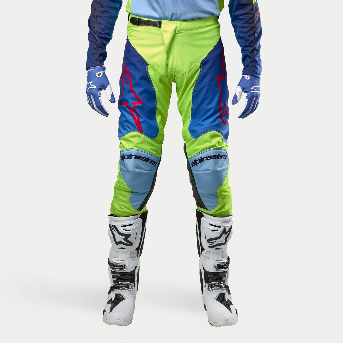 Alpinestars 2024 Racer Hoen Pants, Motocross Pants, Yellow Fluo and Blue Night Navy, worn with white and black motocross boots and blue gloves, featuring bold red logos, light blue knee panels, and a sporty ergonomic design for off-road riding