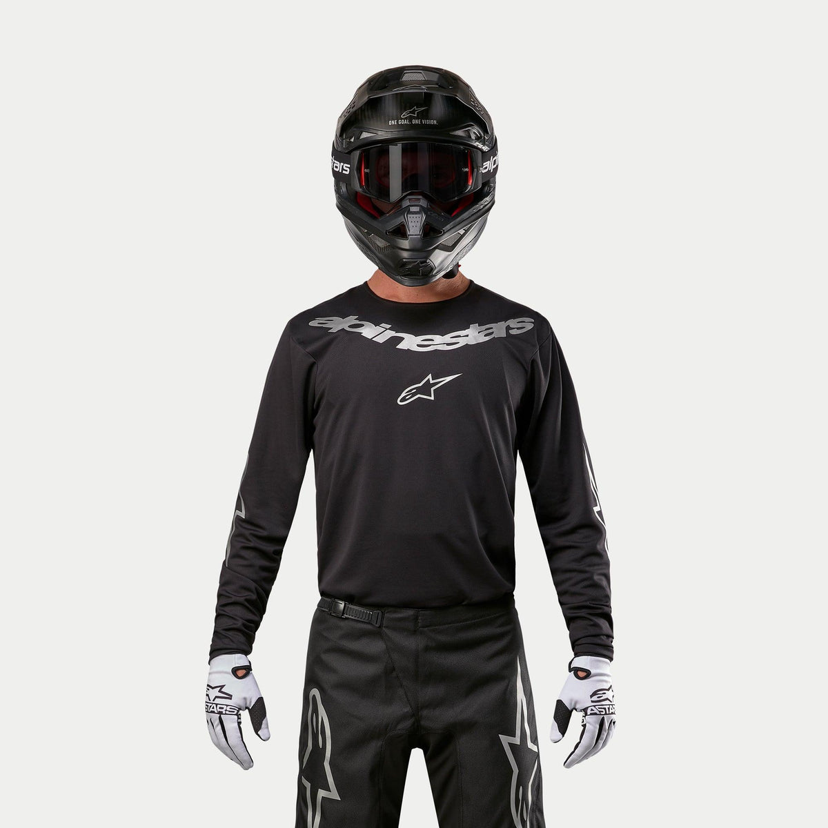 Alpinestars 2024 Fluid Graphite Jersey, Black and Silver motocross jersey, worn by a rider with a black helmet and red goggles, featuring silver Alpinestars branding on the chest, coordinated with black pants and white gloves for off-road performance.