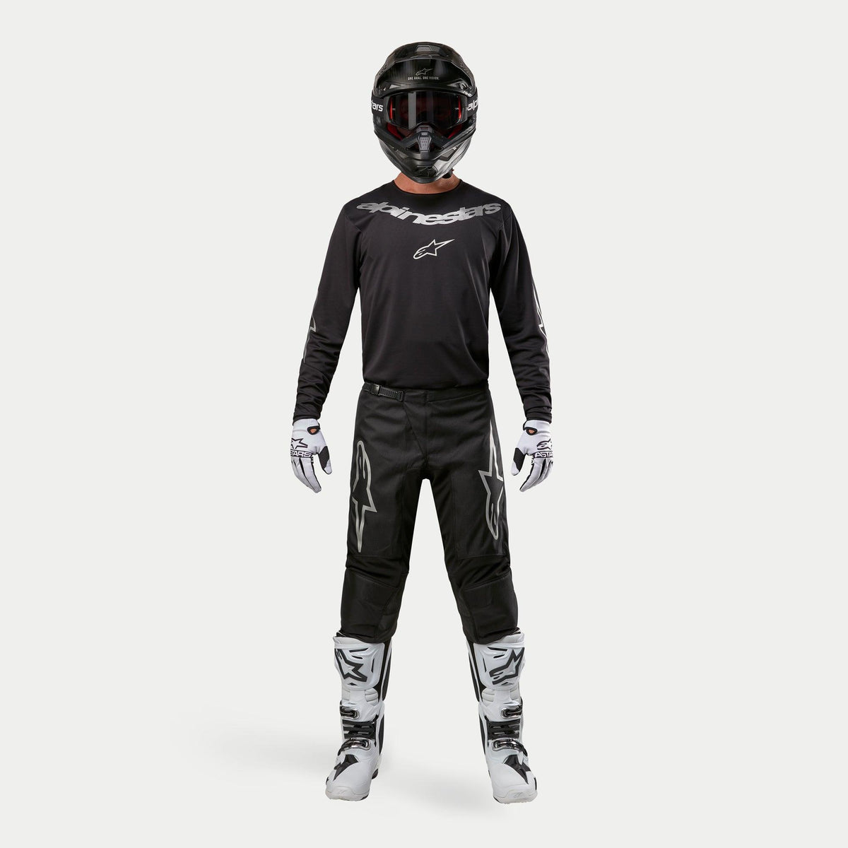 Motocross rider wearing complete racing gear, Alpinestars 2024 Fluid Graphite Jersey in Black Silver, black pants with silver star logos, black helmet with red goggles, white and black boots, white and black gloves, coordinated motocross outfit