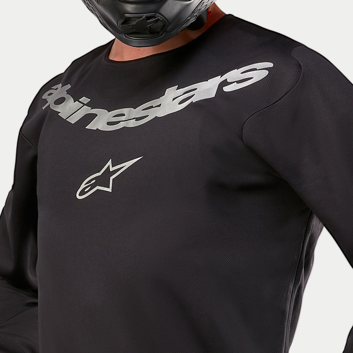 Alpinestars 2024 Fluid Graphite Jersey, Motocross Jersey, Black and Silver, close-up detail of the chest area featuring silver Alpinestars branding and star logo, breathable poly-fabric construction, worn by a rider in a black helmet