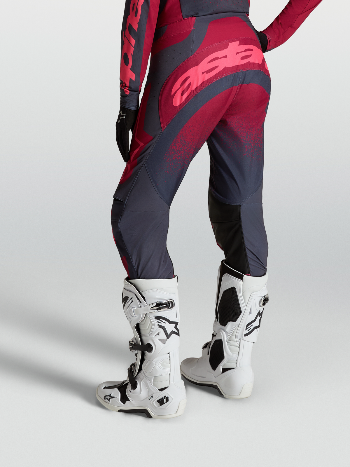 Alpinestars Stella Techstar Swan Pants shown from behind, featuring Crimson and Dark Gray textile panels, paired with white Tech 10 motocross boots.